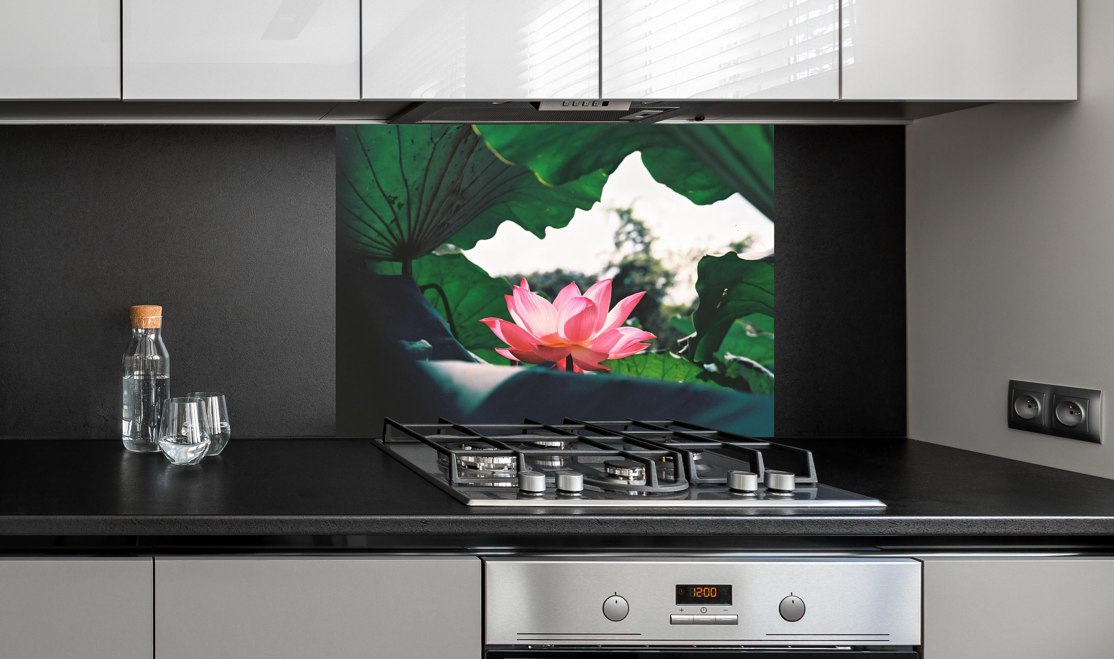 Spritzschutz - Lotosblume inmitten von Blättern hinter einem Cerankochfeld zwischen Holz-Kochutensilien
