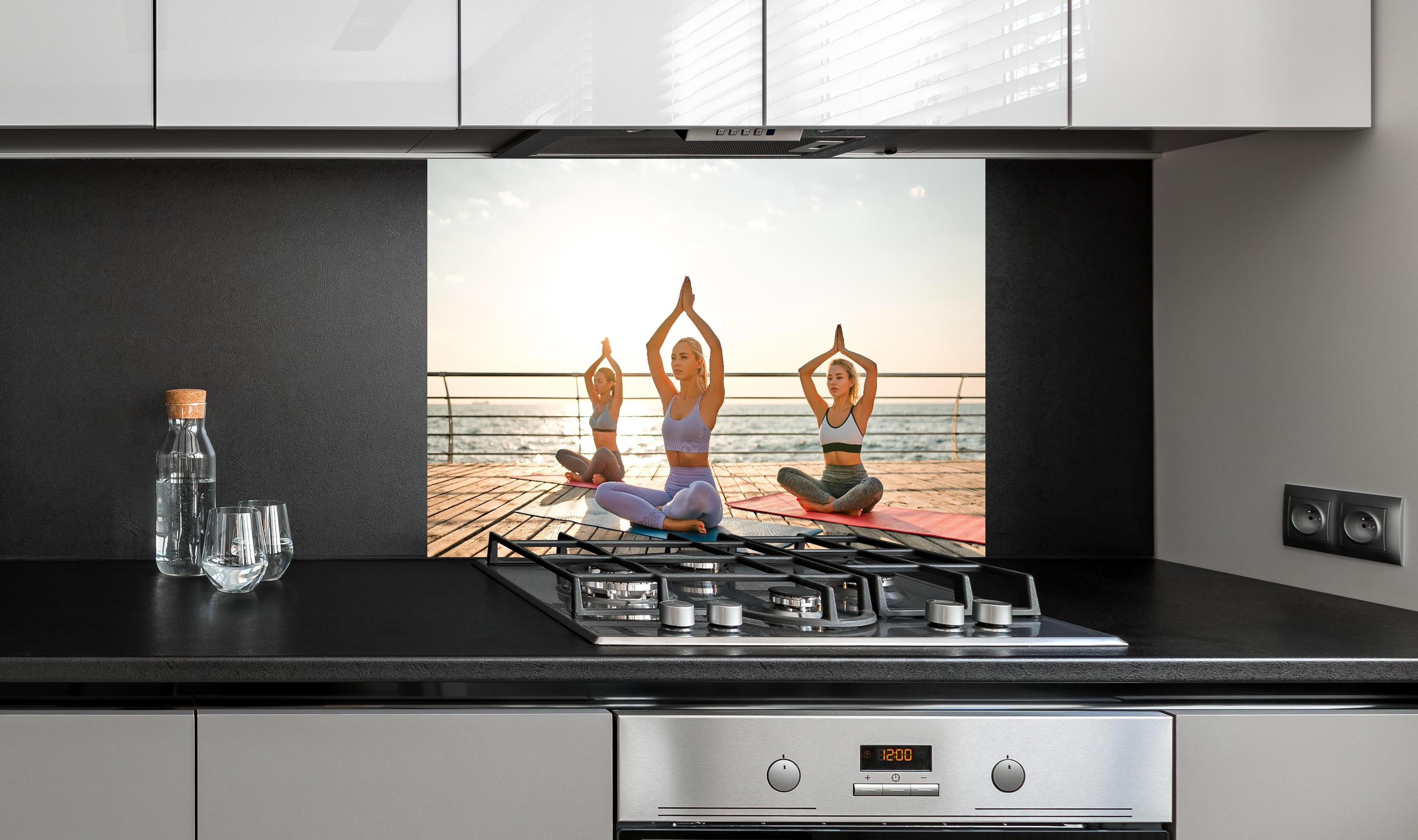 Spritzschutz - Mädchen beim Yoga am Morgen hinter einem Cerankochfeld zwischen Holz-Kochutensilien
