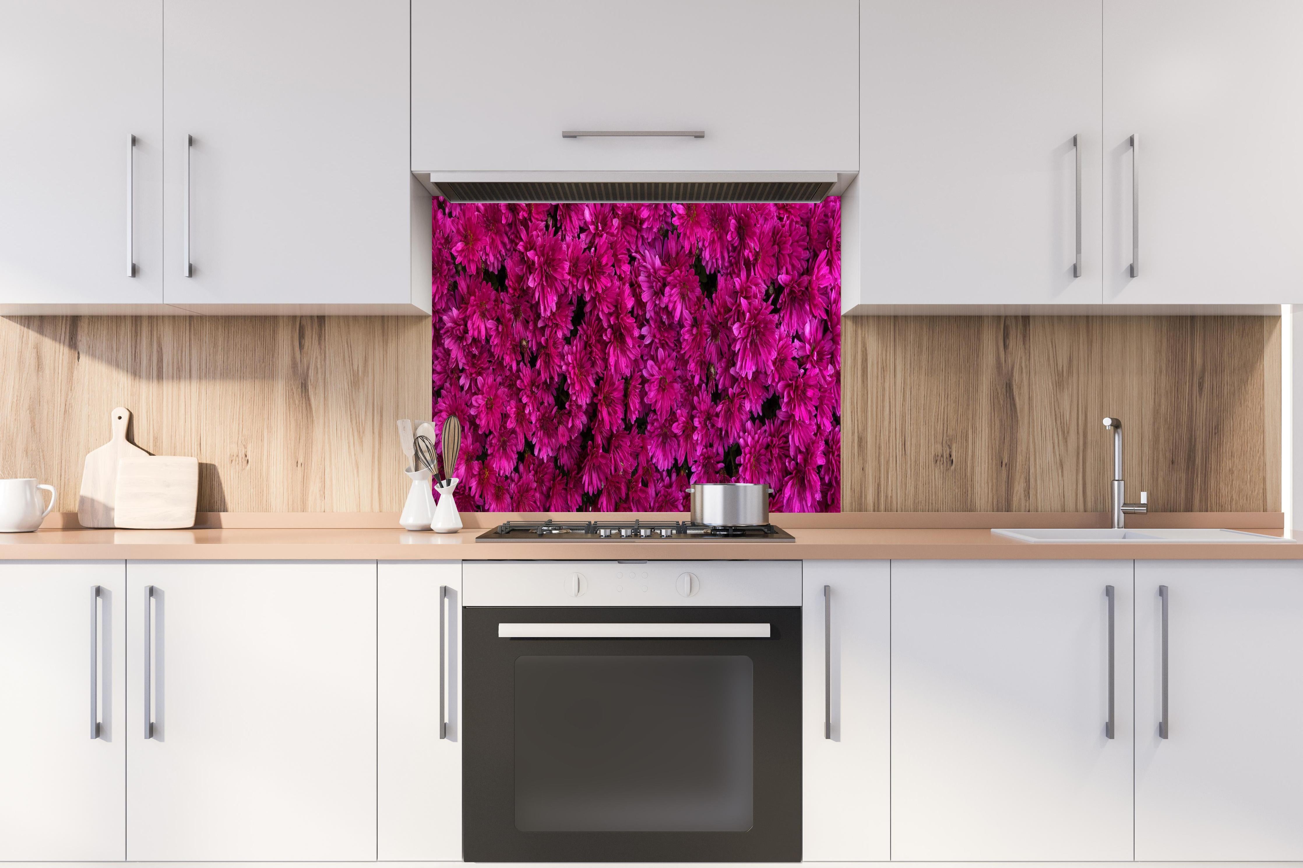 Spritzschutz - Magenta Blüten von Chrysanthemen hinter einem Cerankochfeld zwischen Holz-Kochutensilien
