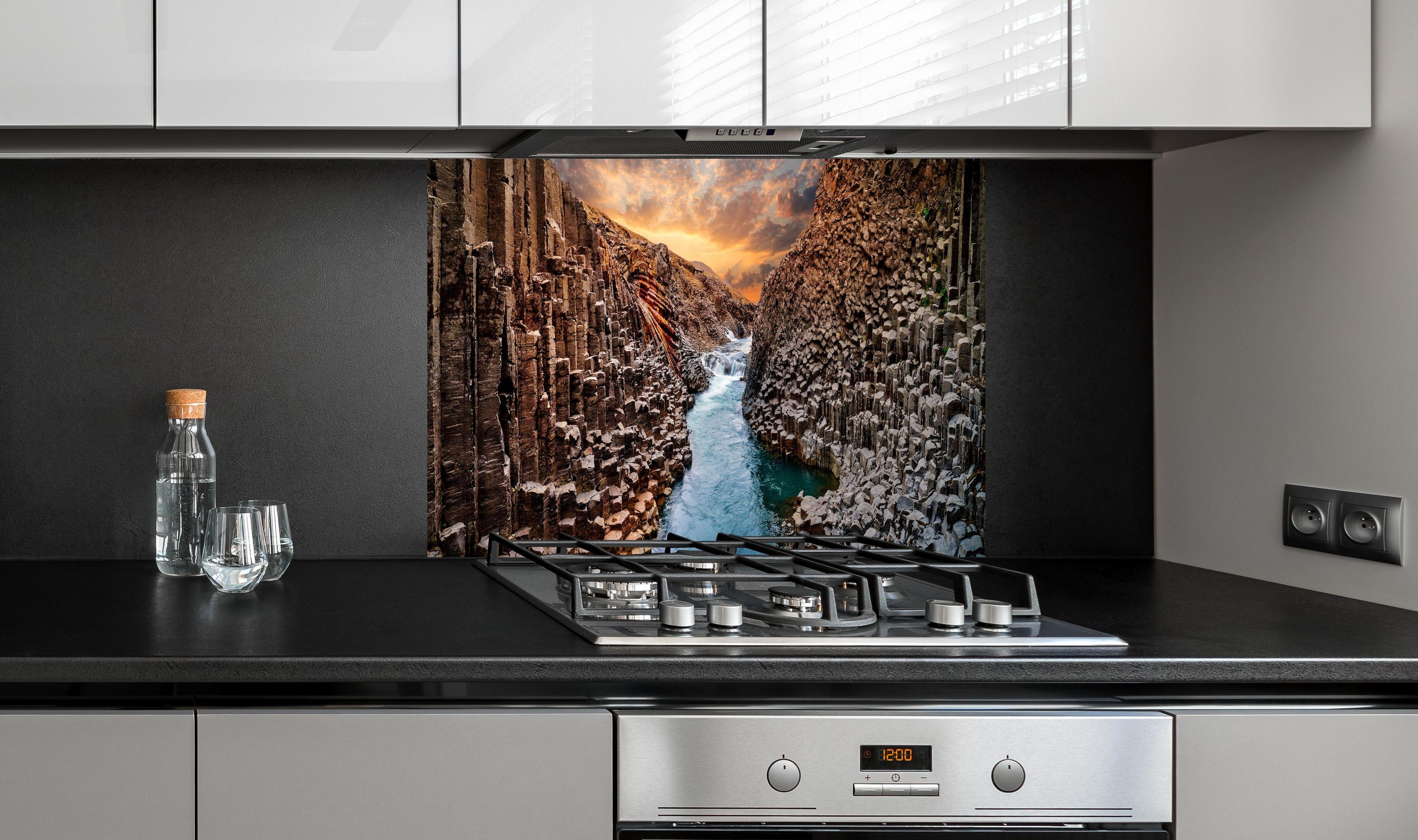 Spritzschutz - Majestätische Basalt-Schlucht Island Sonnenuntergang hinter einem Cerankochfeld zwischen Holz-Kochutensilien
