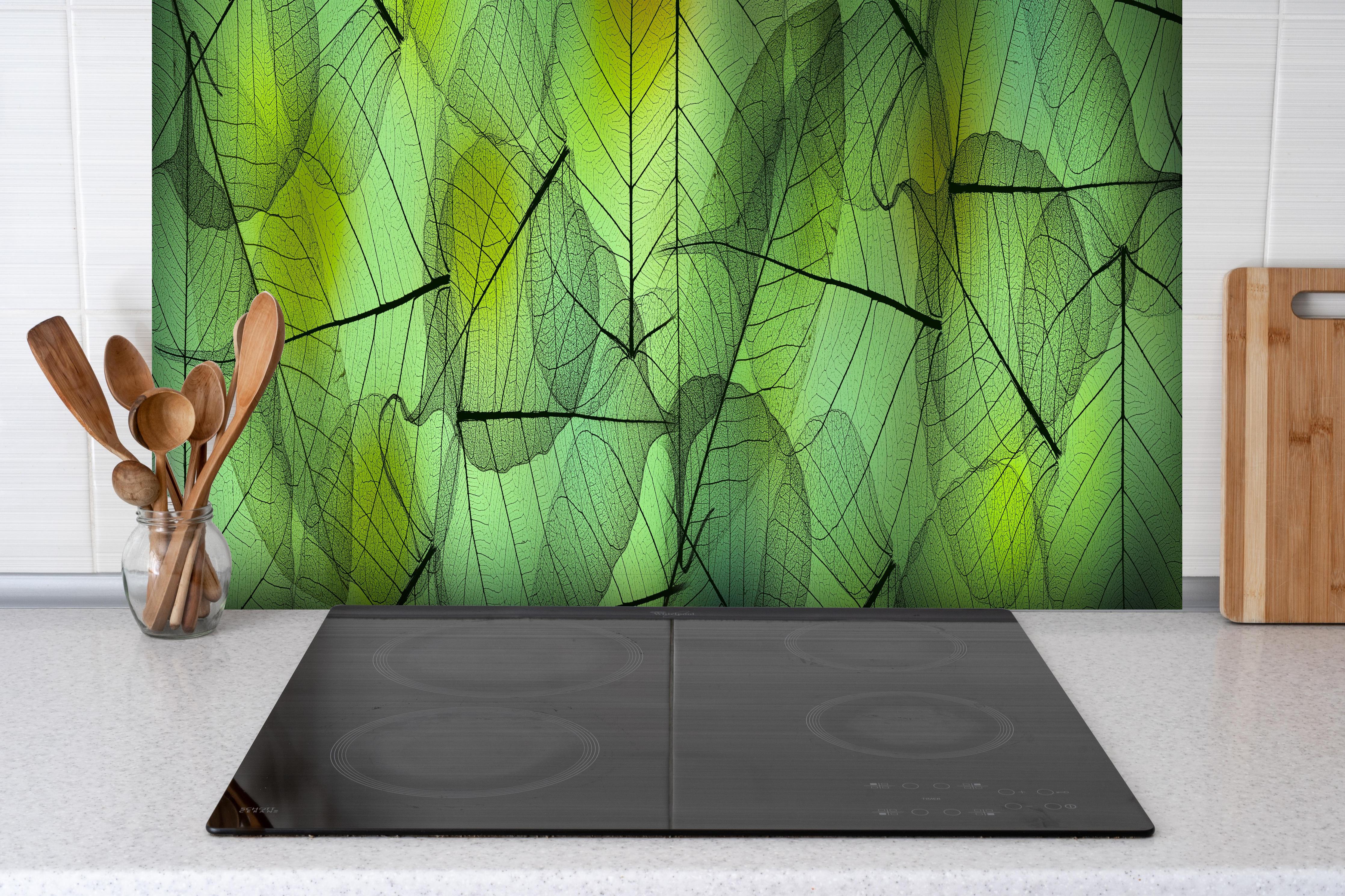 Spritzschutz - Makroaufnahme Blattadern in Grün und Gelb hinter einem Cerankochfeld zwischen Holz-Kochutensilien
