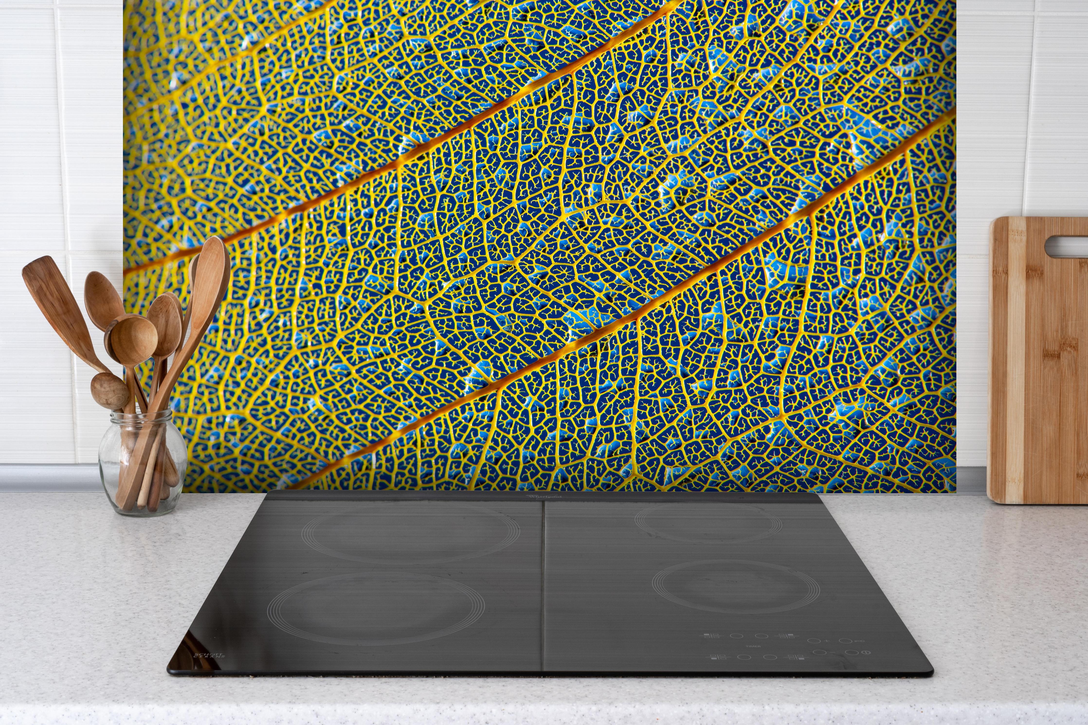 Spritzschutz - Makroaufnahme Gelbes Blatt mit Adern hinter einem Cerankochfeld zwischen Holz-Kochutensilien
