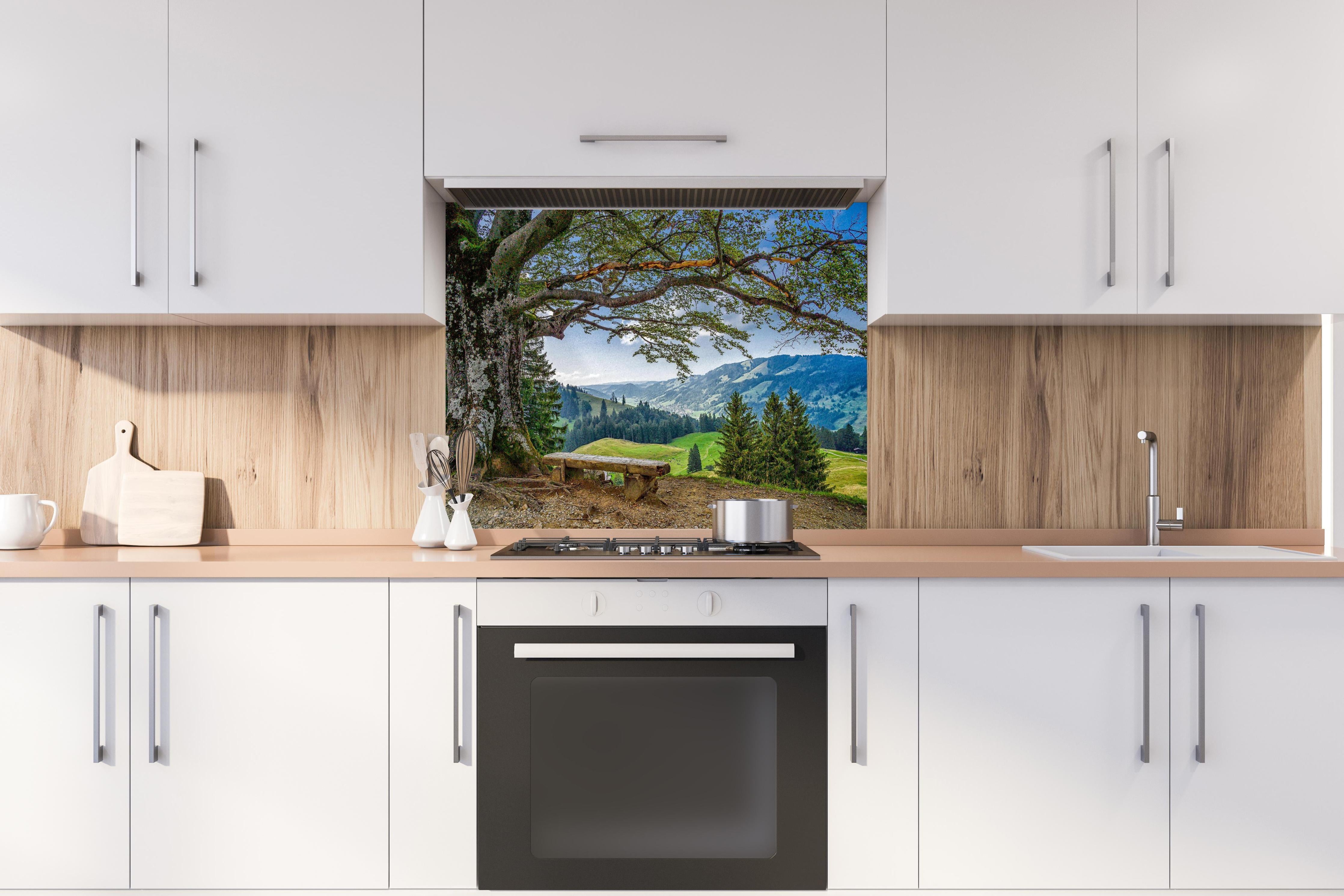 Spritzschutz - Malersche Bergpanorama mit alter Baum hinter einem Cerankochfeld zwischen Holz-Kochutensilien
