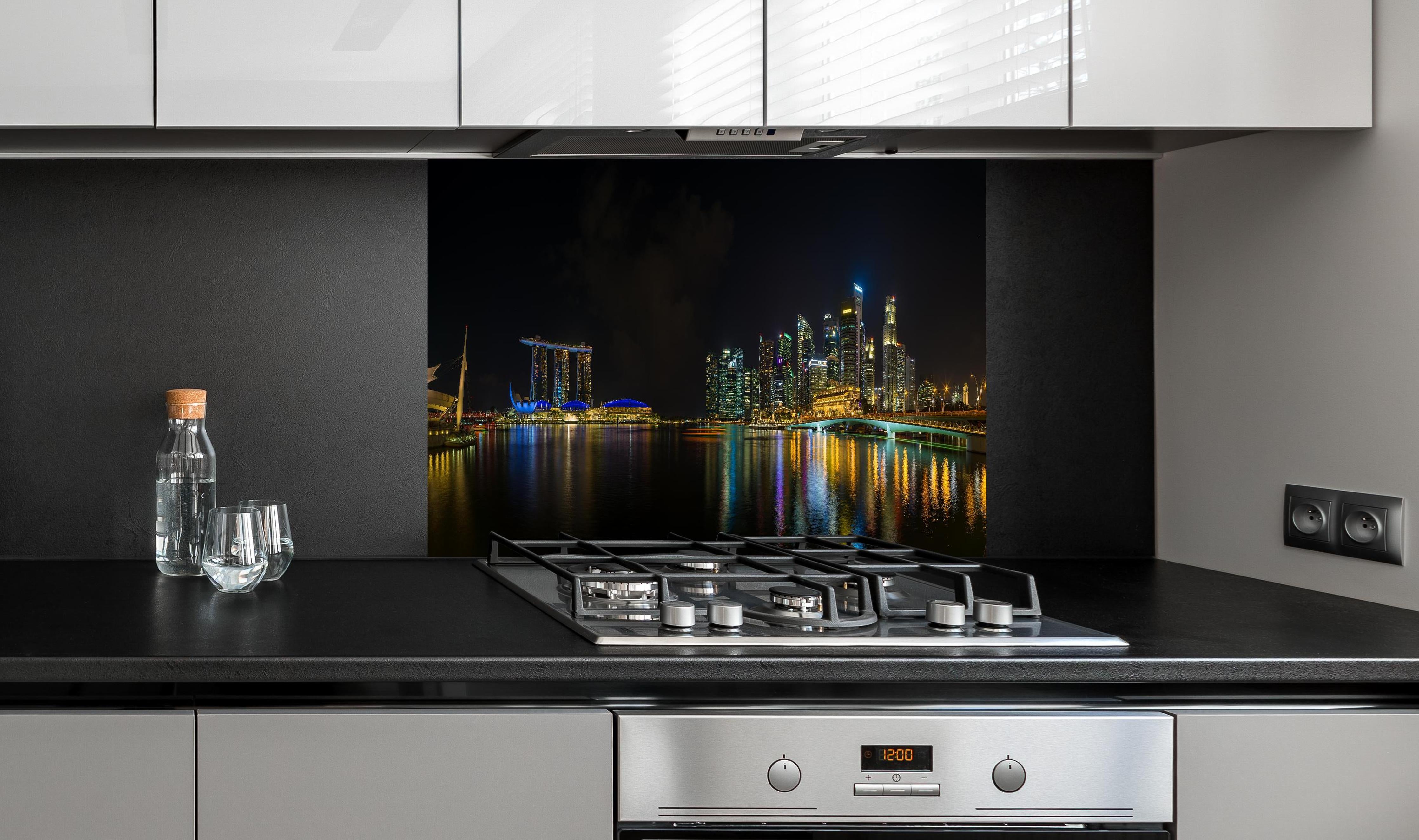 Spritzschutz - Marina Bay Sands bei Nacht hinter einem Cerankochfeld zwischen Holz-Kochutensilien
