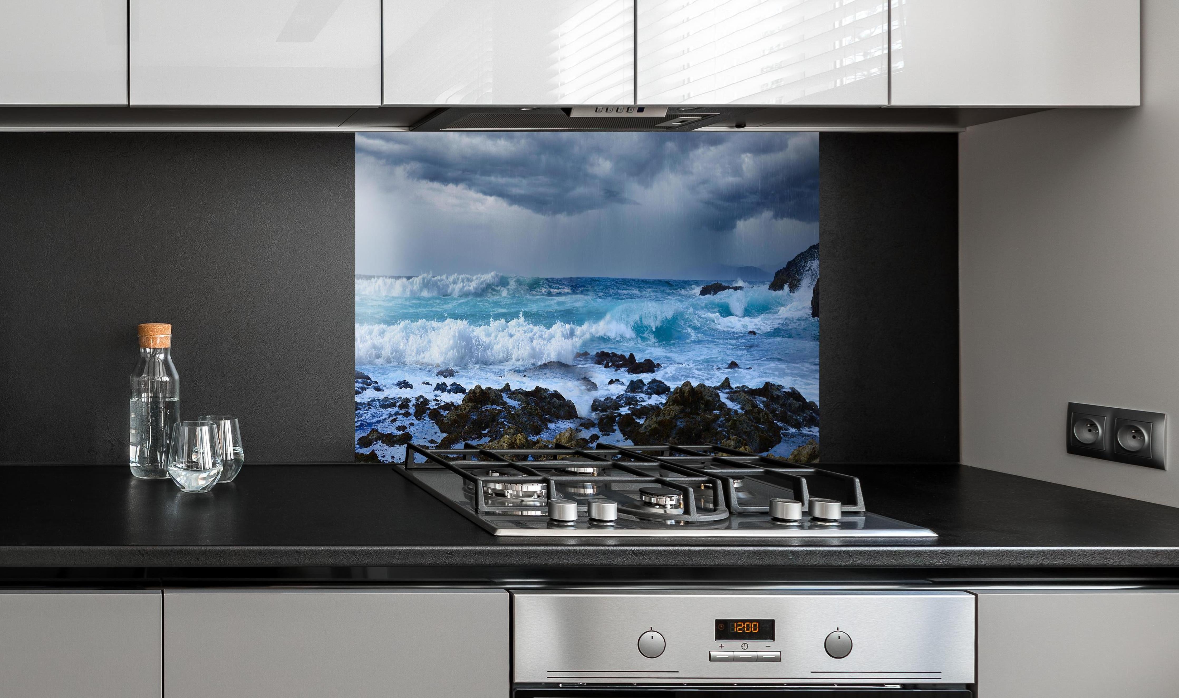 Spritzschutz - Meeresküste mit dunklen Regenwolken und stürmischer See hinter einem Cerankochfeld zwischen Holz-Kochutensilien
