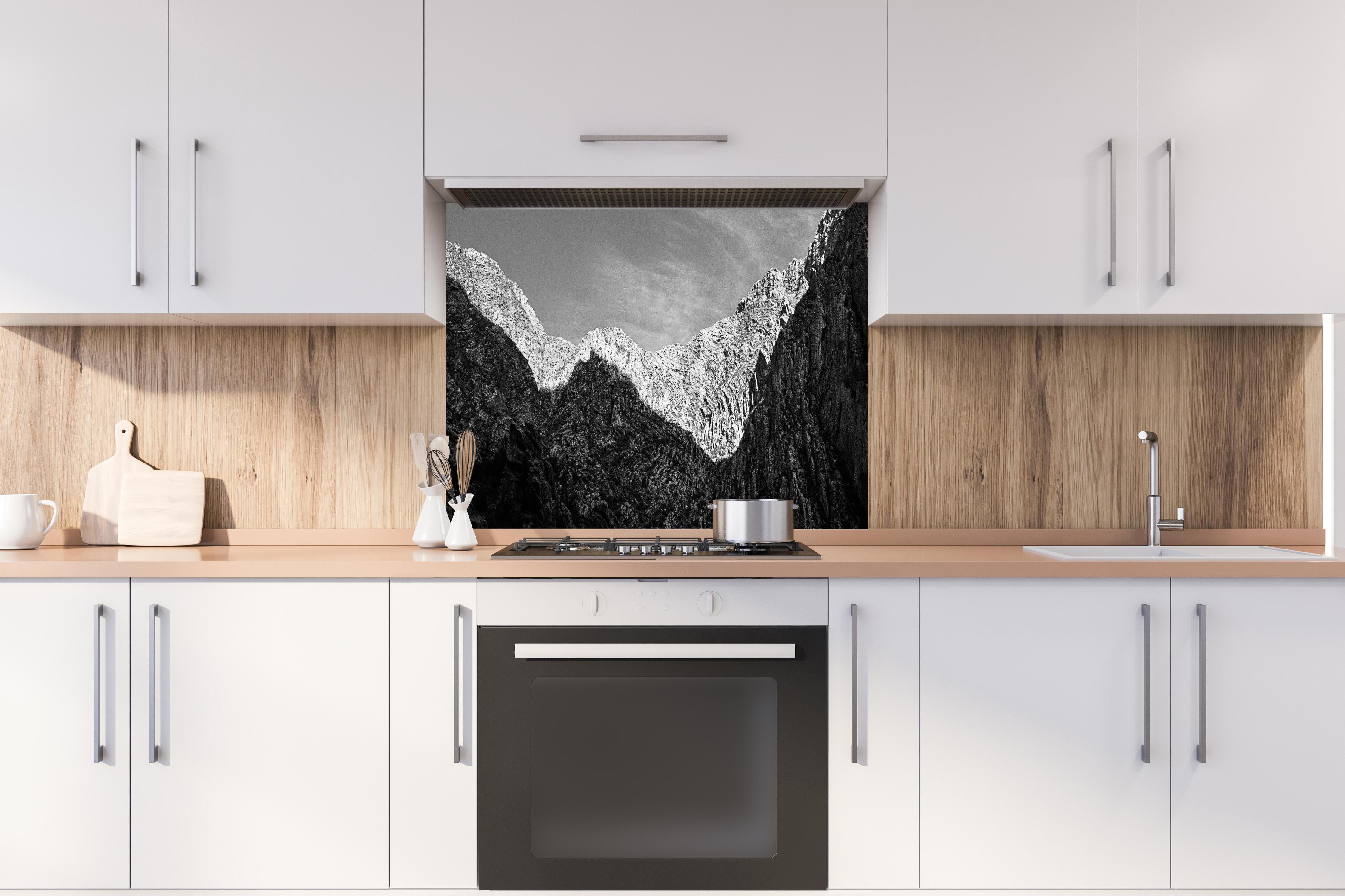 Spritzschutz - Minimalistische Berglandschaft in Schwarz-Weiß hinter einem Cerankochfeld zwischen Holz-Kochutensilien
