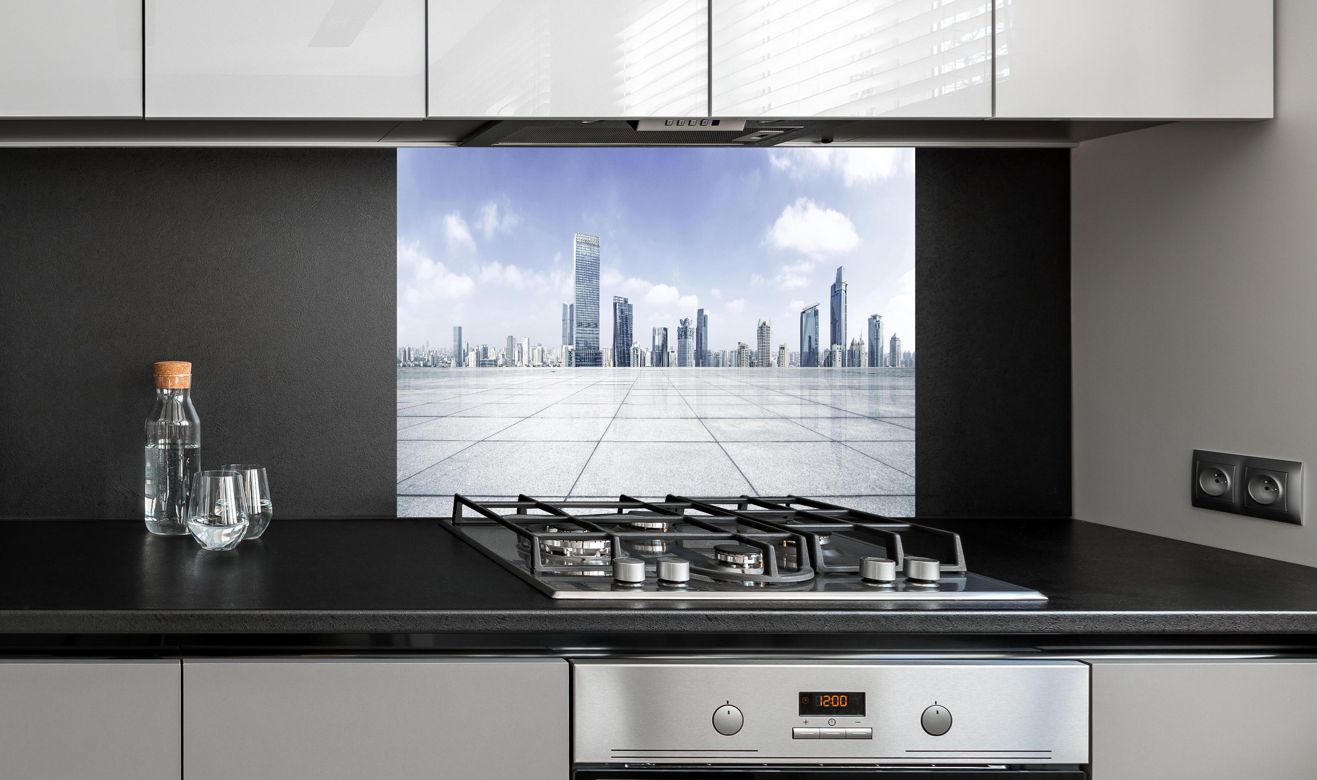 Spritzschutz - Moderner Skyline und Gebäuden hinter einem Cerankochfeld zwischen Holz-Kochutensilien
