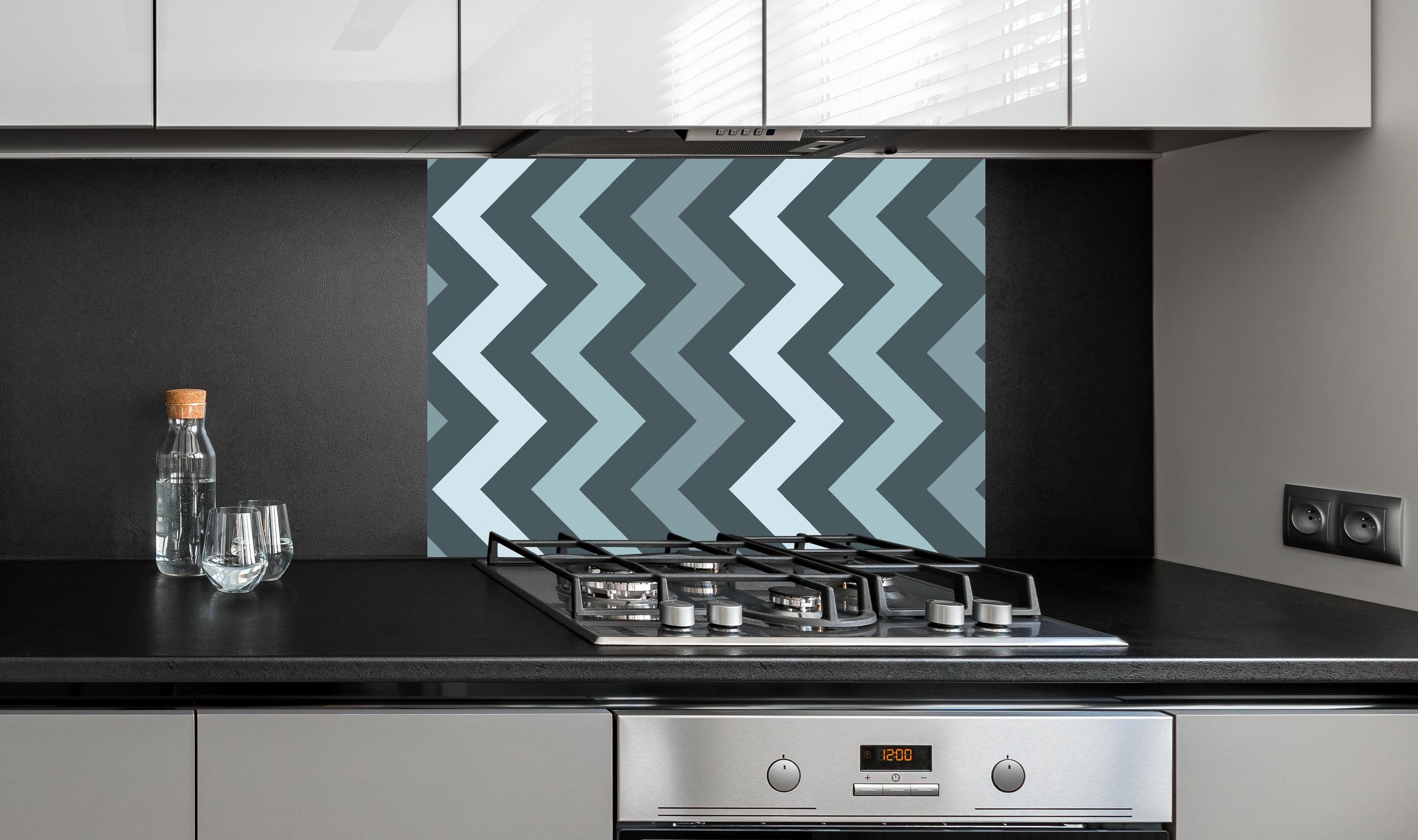 Spritzschutz - Modernes Chevron Design in Grau-Weiß hinter einem Cerankochfeld zwischen Holz-Kochutensilien
