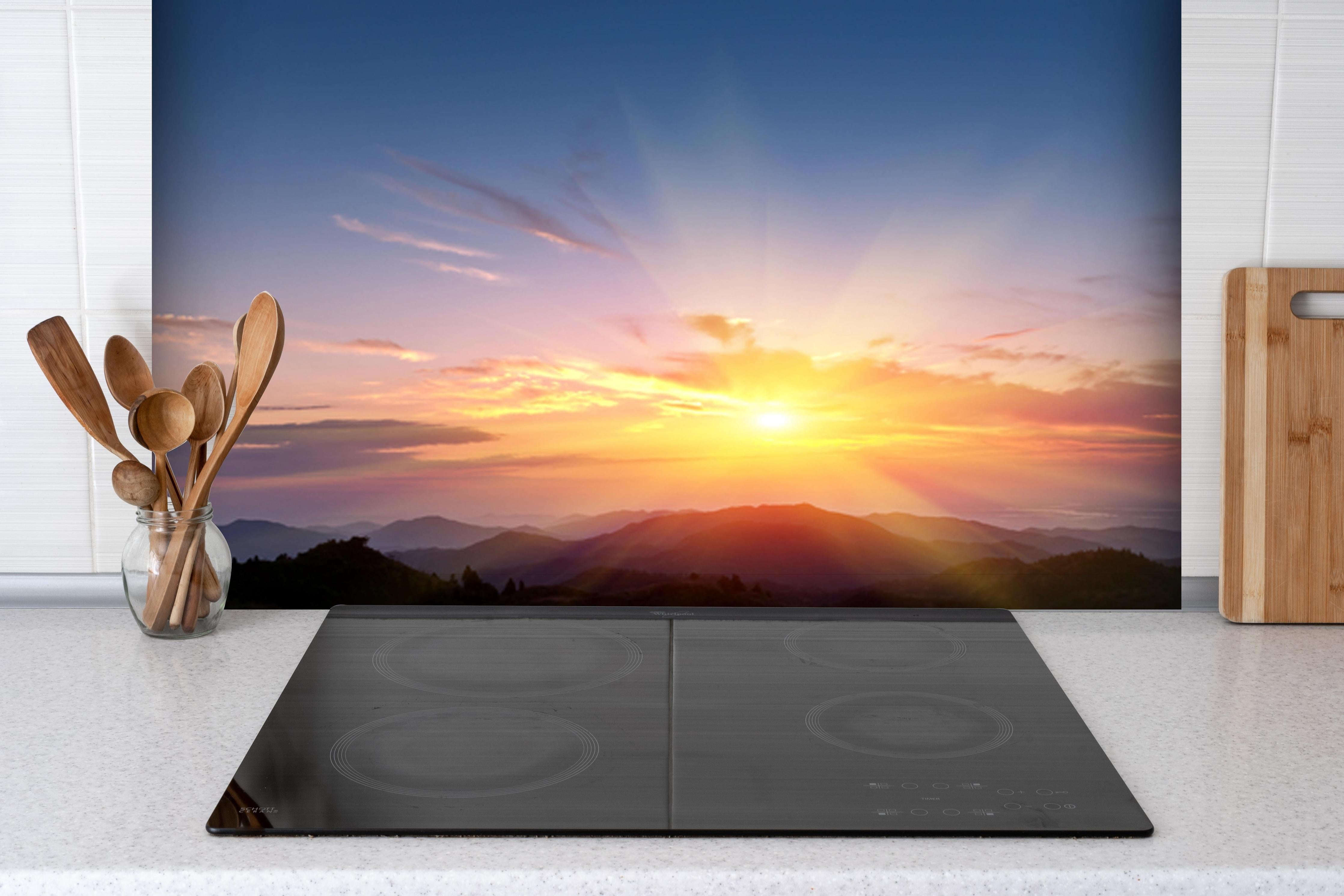 Spritzschutz - Morgendämmerung über Berglandschaft hinter einem Cerankochfeld zwischen Holz-Kochutensilien
