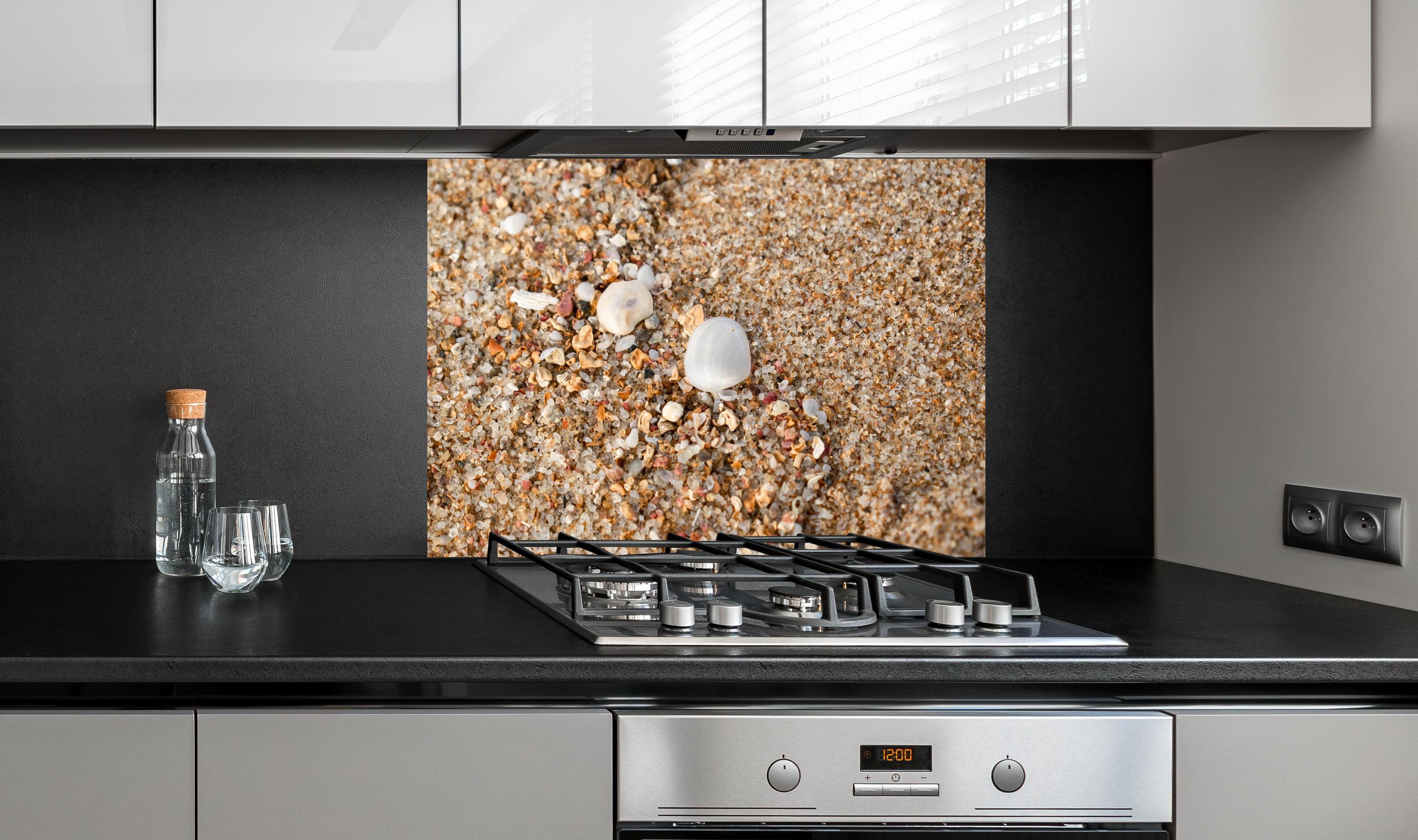 Spritzschutz - Muscheln im Strandsand. Shell hinter einem Cerankochfeld zwischen Holz-Kochutensilien
