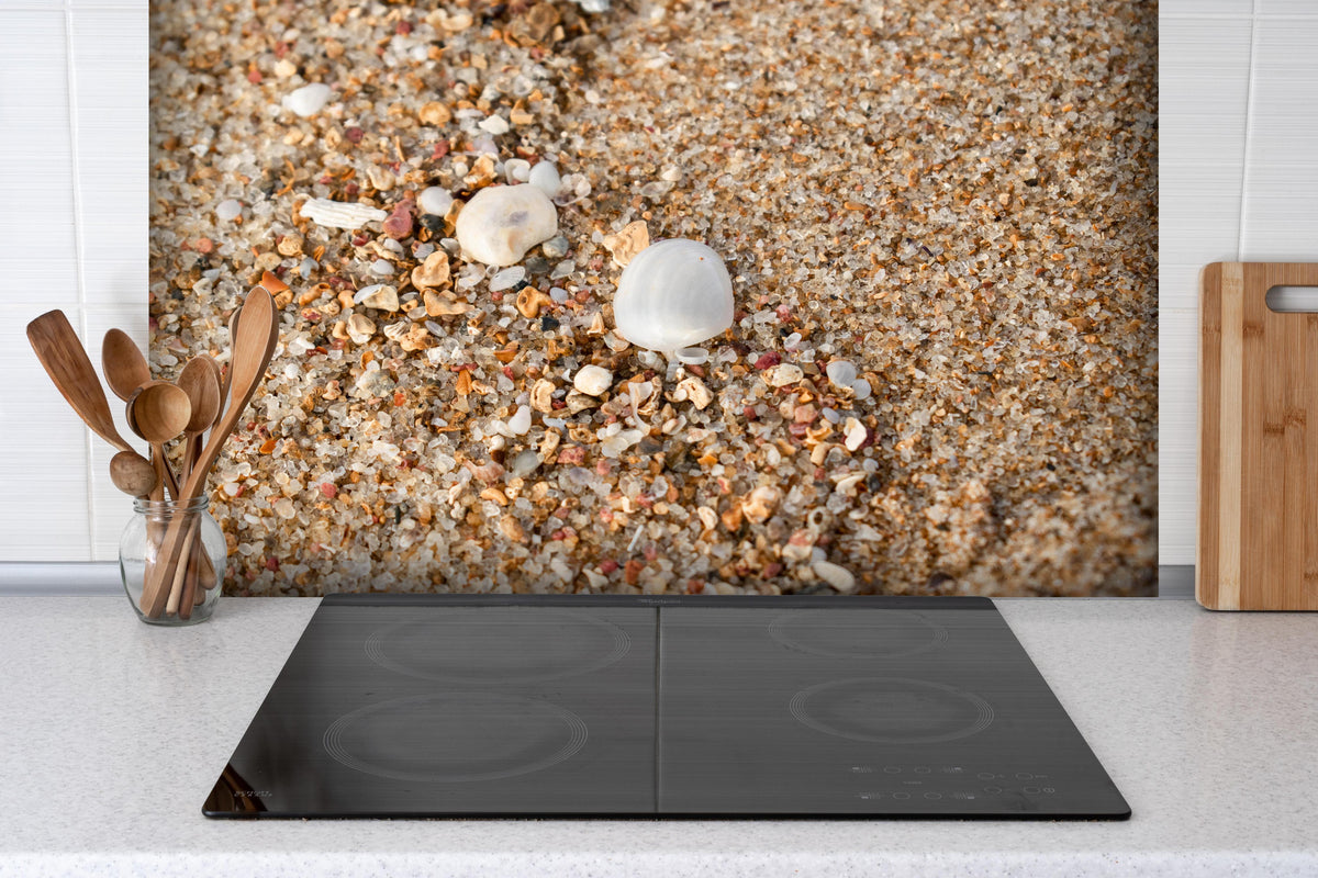 Spritzschutz - Muscheln im Strandsand. Shell hinter einem Cerankochfeld zwischen Holz-Kochutensilien
