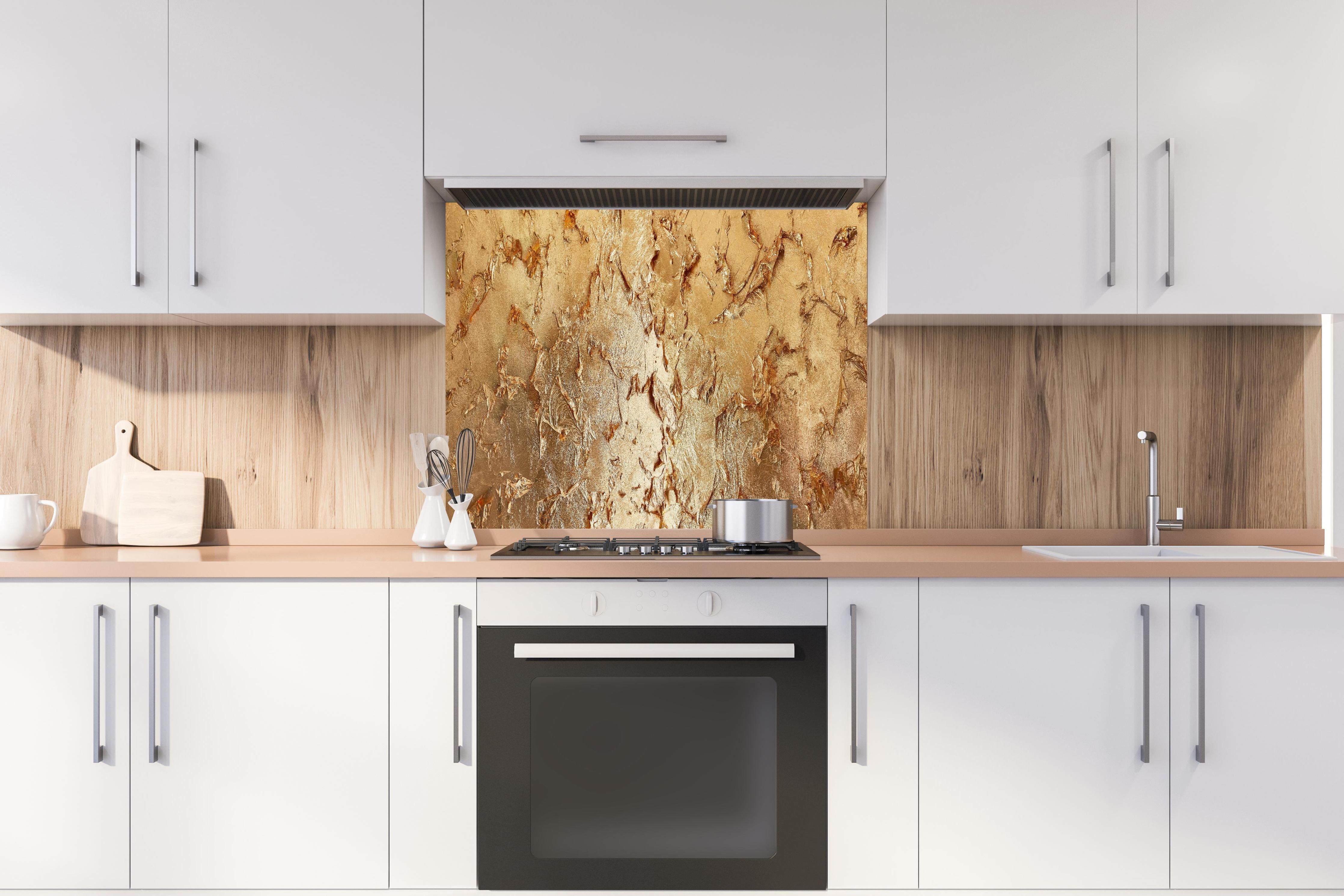 Spritzschutz - Muster einer vergoldeten Wand hinter einem Cerankochfeld zwischen Holz-Kochutensilien
