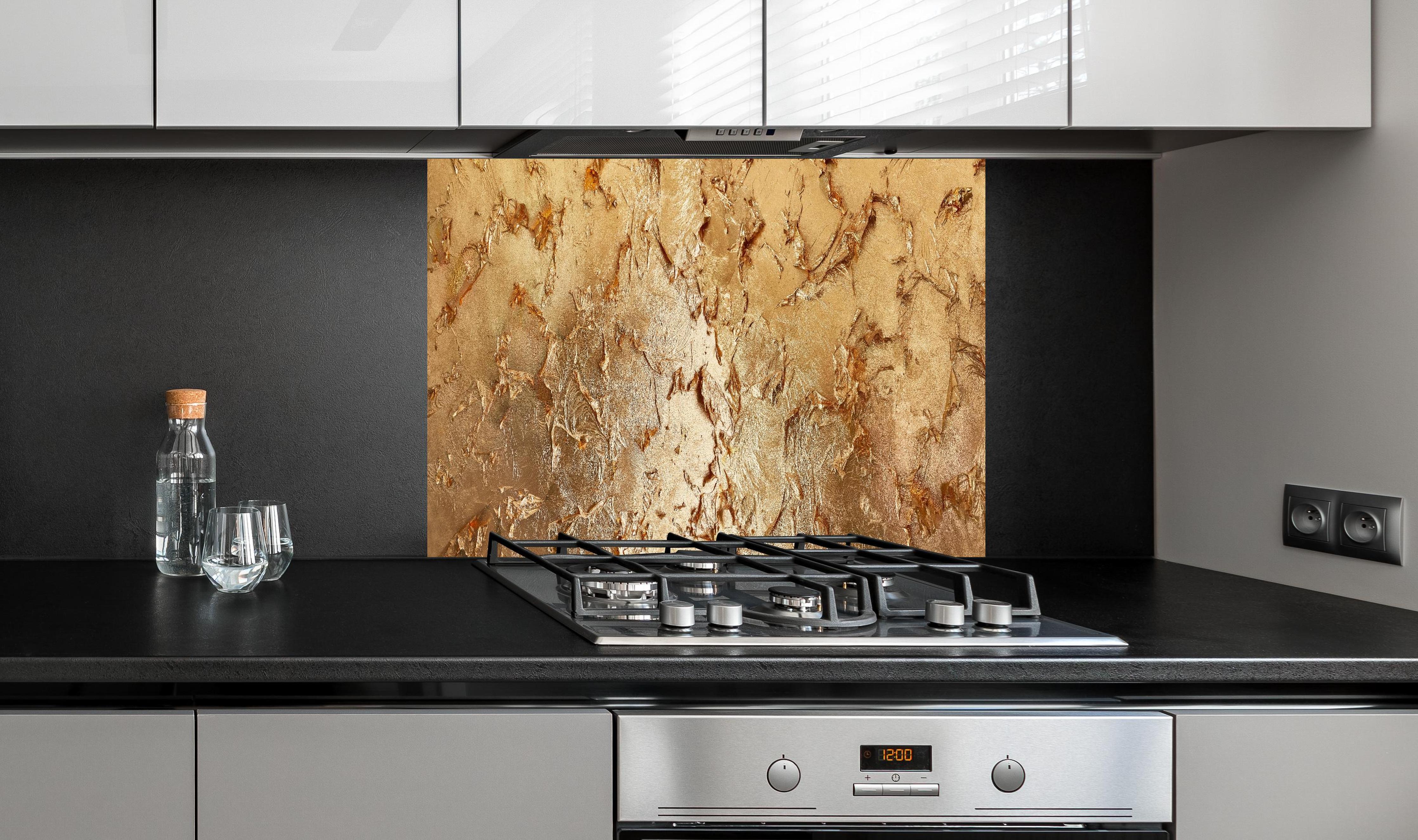 Spritzschutz - Muster einer vergoldeten Wand hinter einem Cerankochfeld zwischen Holz-Kochutensilien
