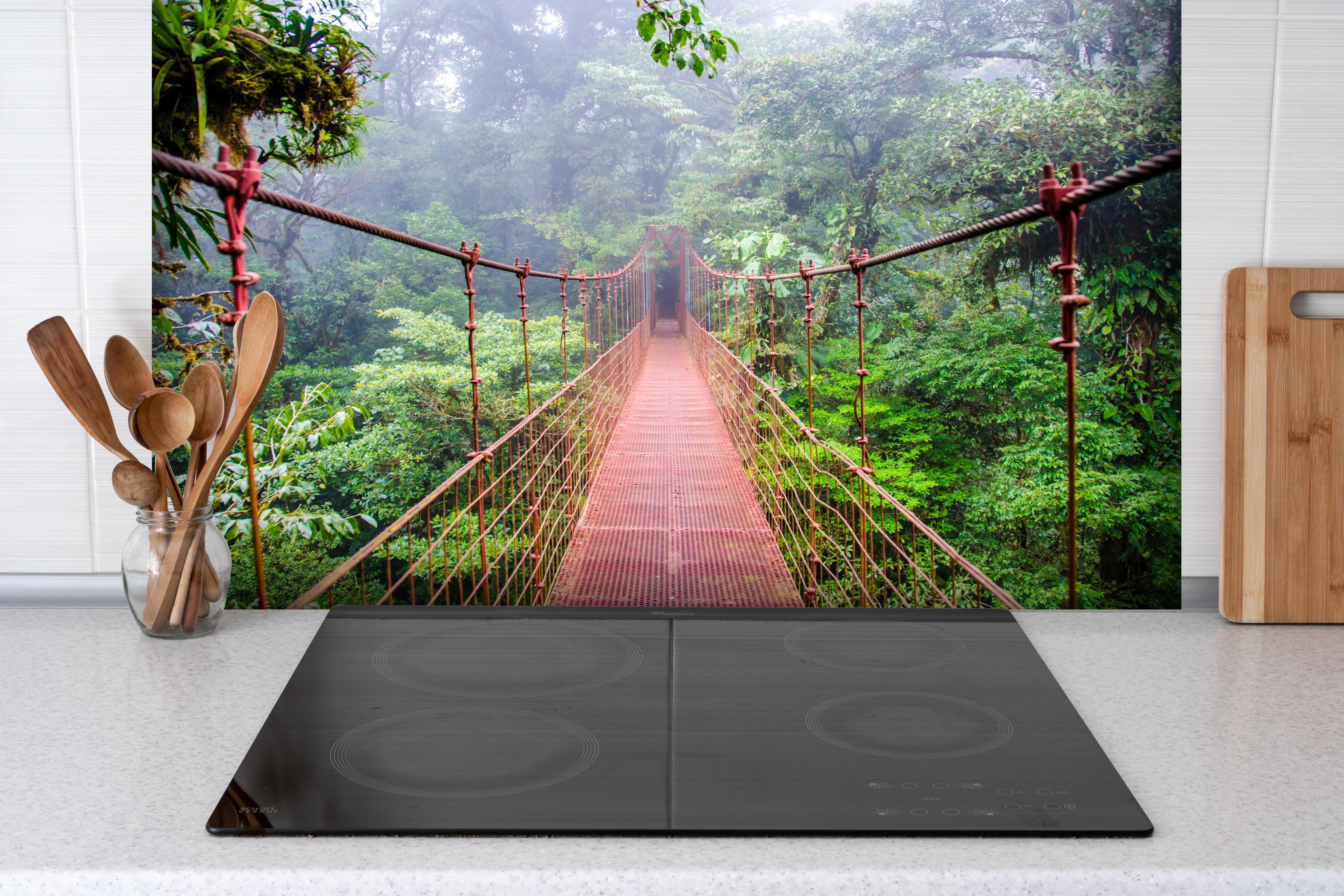 Spritzschutz - Mystische Hängebrücke im nebeligen Regenwald hinter einem Cerankochfeld zwischen Holz-Kochutensilien
