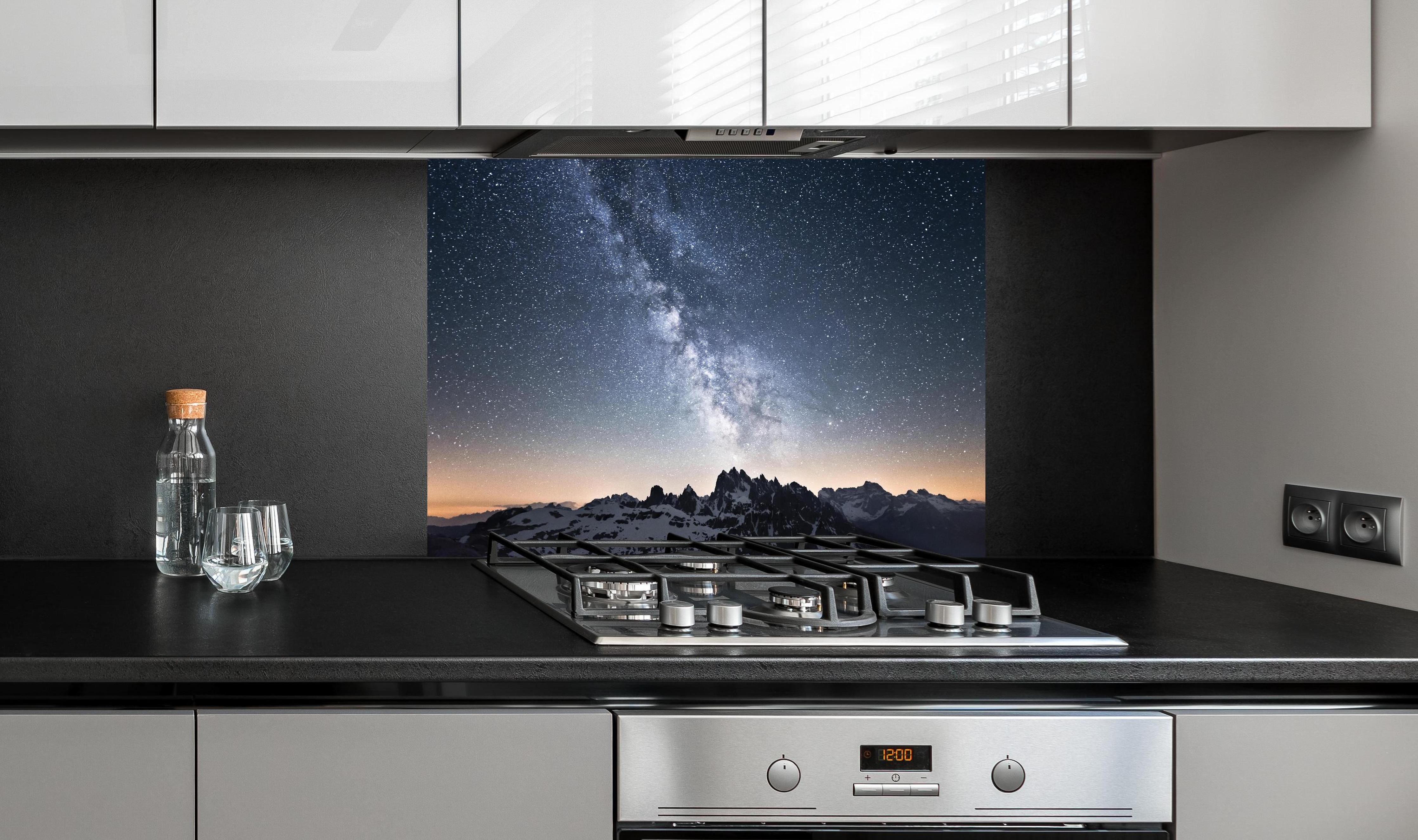 Spritzschutz - Nachthimmel Sterne Schneeberge Panorama hinter einem Cerankochfeld zwischen Holz-Kochutensilien
