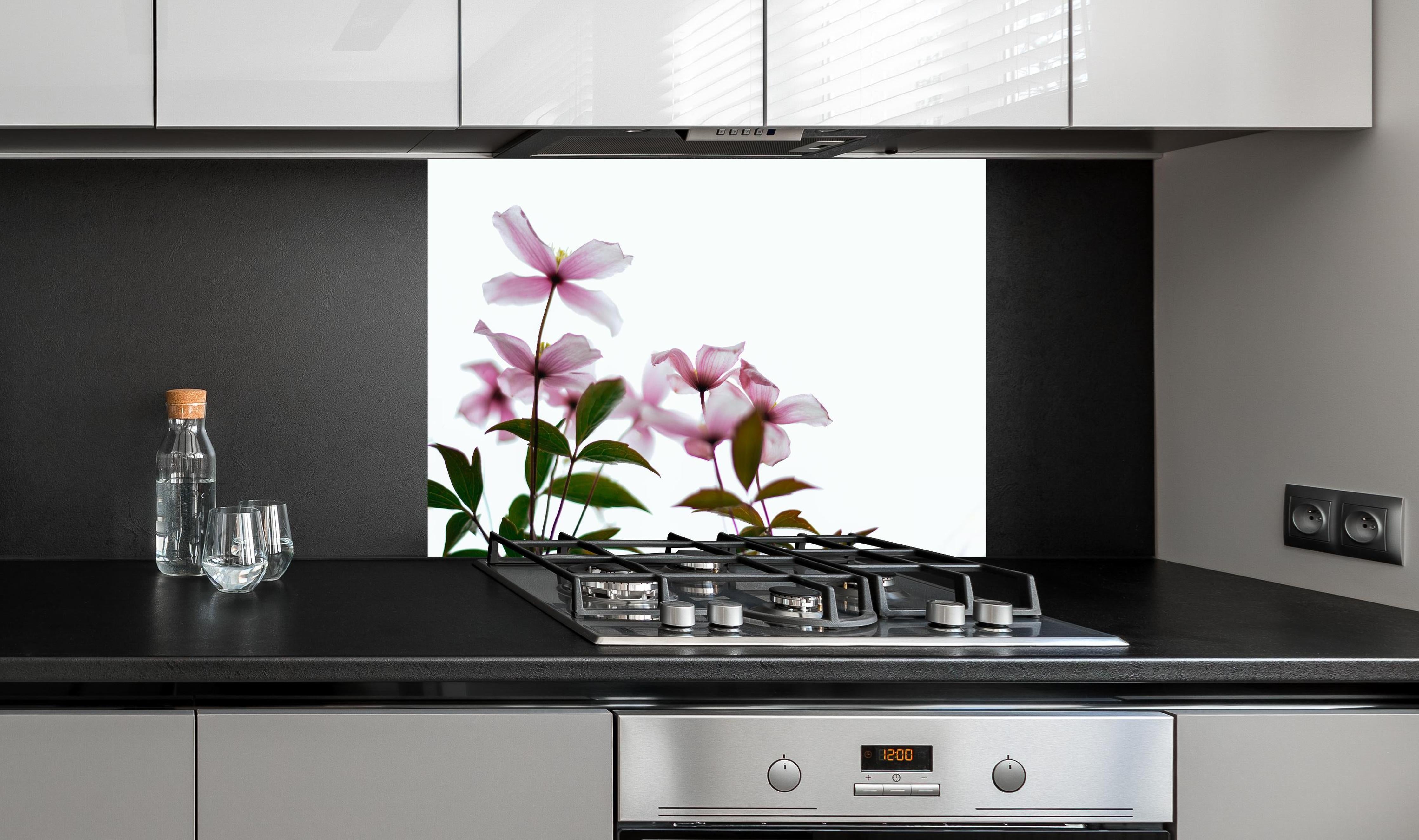 Spritzschutz - Nahaufnahme - Clematis Blüten hinter einem Cerankochfeld zwischen Holz-Kochutensilien
