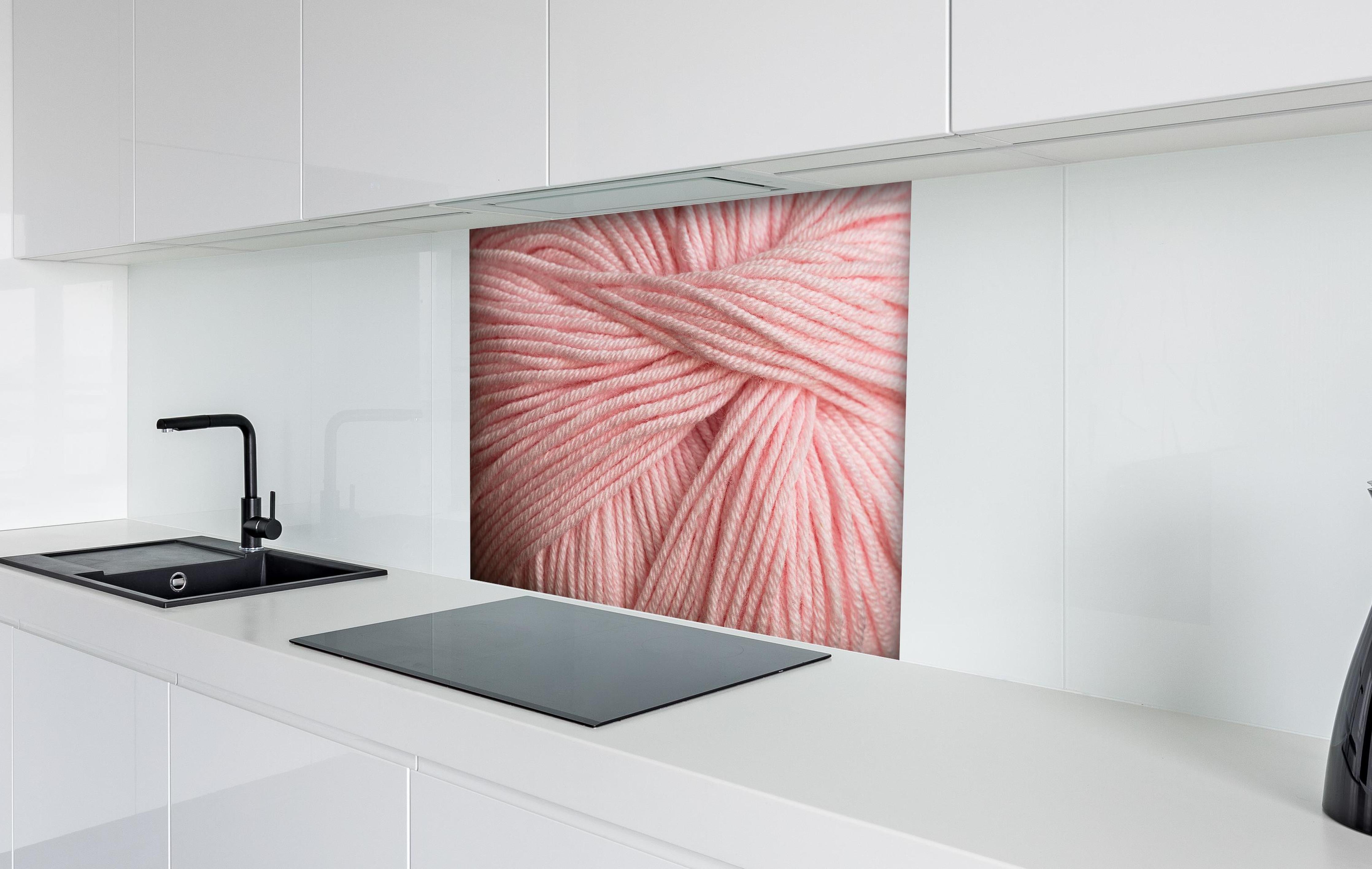 Spritzschutz - Nahaufnahme eines rosa Garnknäuels hinter einem Cerankochfeld zwischen Holz-Kochutensilien
