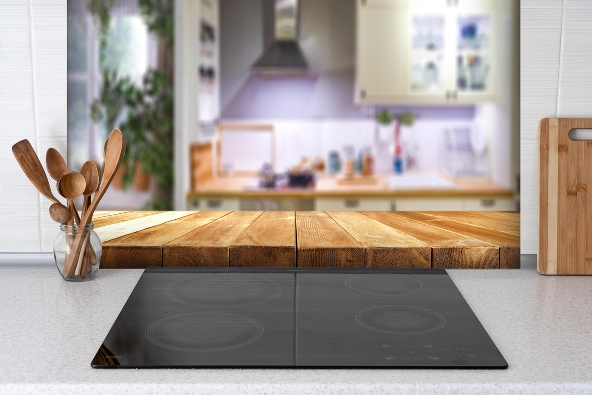 Spritzschutz - Naturholz Tischplatte vor Kücheninterieur hinter einem Cerankochfeld zwischen Holz-Kochutensilien
