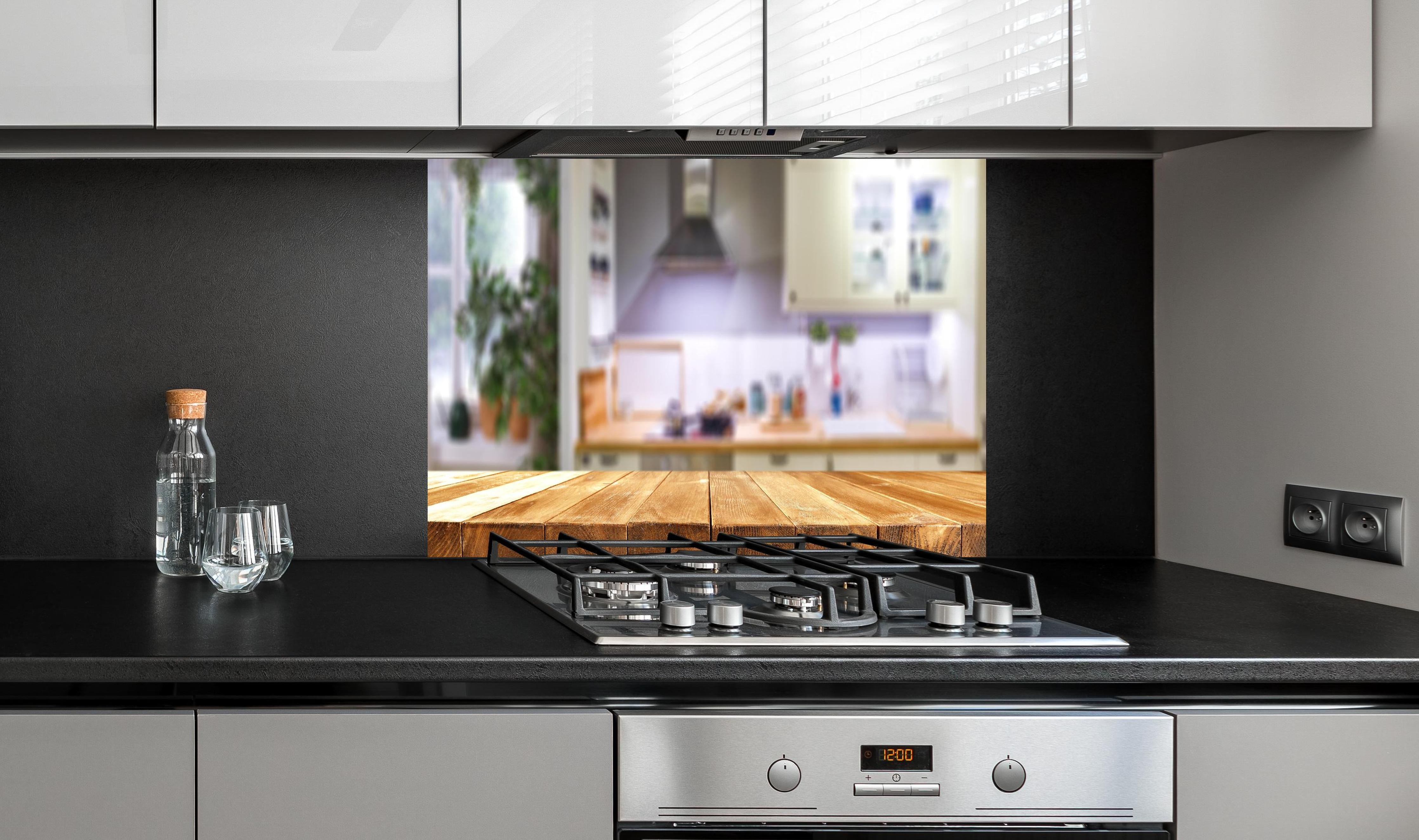 Spritzschutz - Naturholz Tischplatte vor Kücheninterieur hinter einem Cerankochfeld zwischen Holz-Kochutensilien

