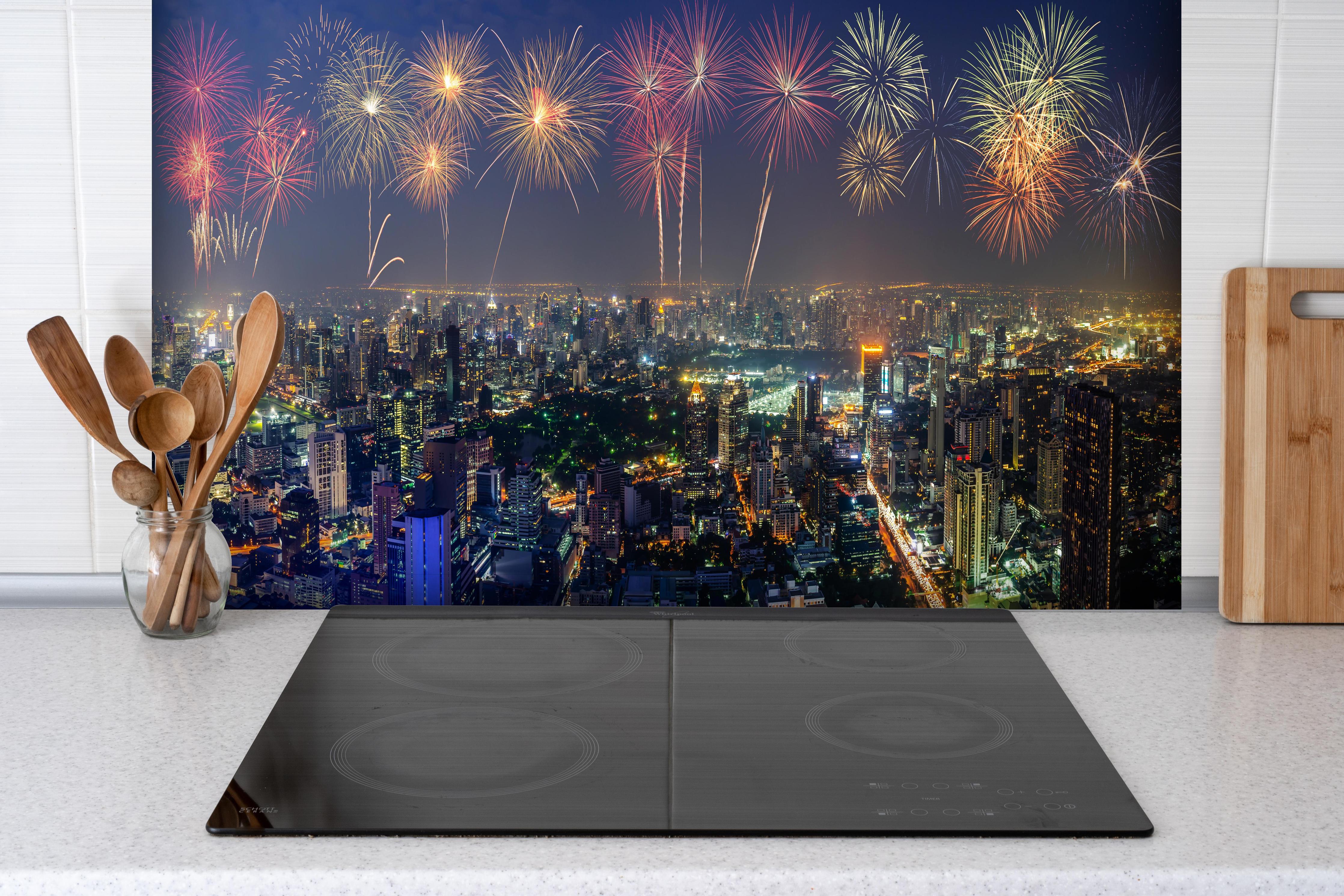 Spritzschutz - Neujahres Skyline in Bangkok hinter einem Cerankochfeld zwischen Holz-Kochutensilien
