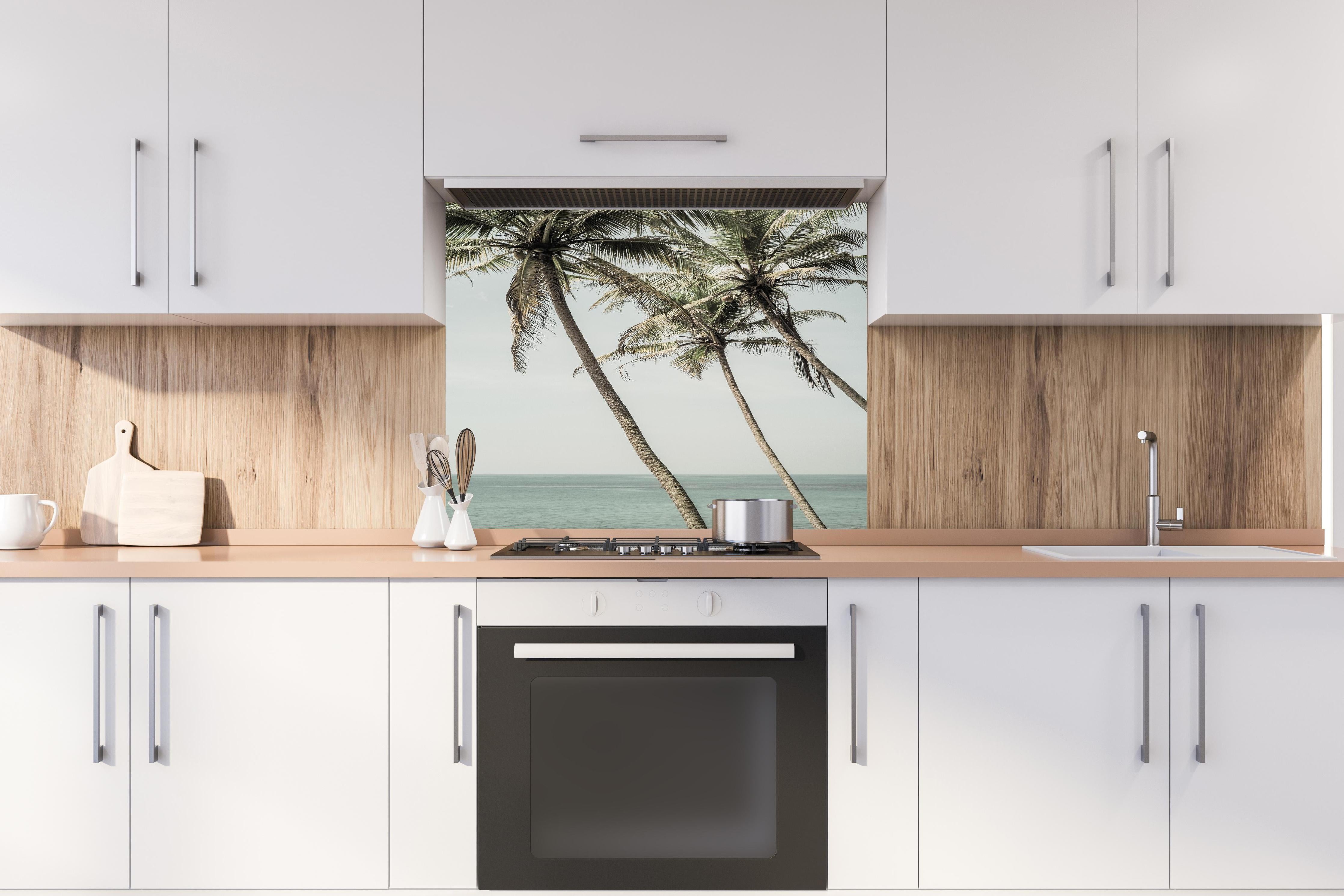 Spritzschutz - Palmen am Meer hinter einem Cerankochfeld zwischen Holz-Kochutensilien
