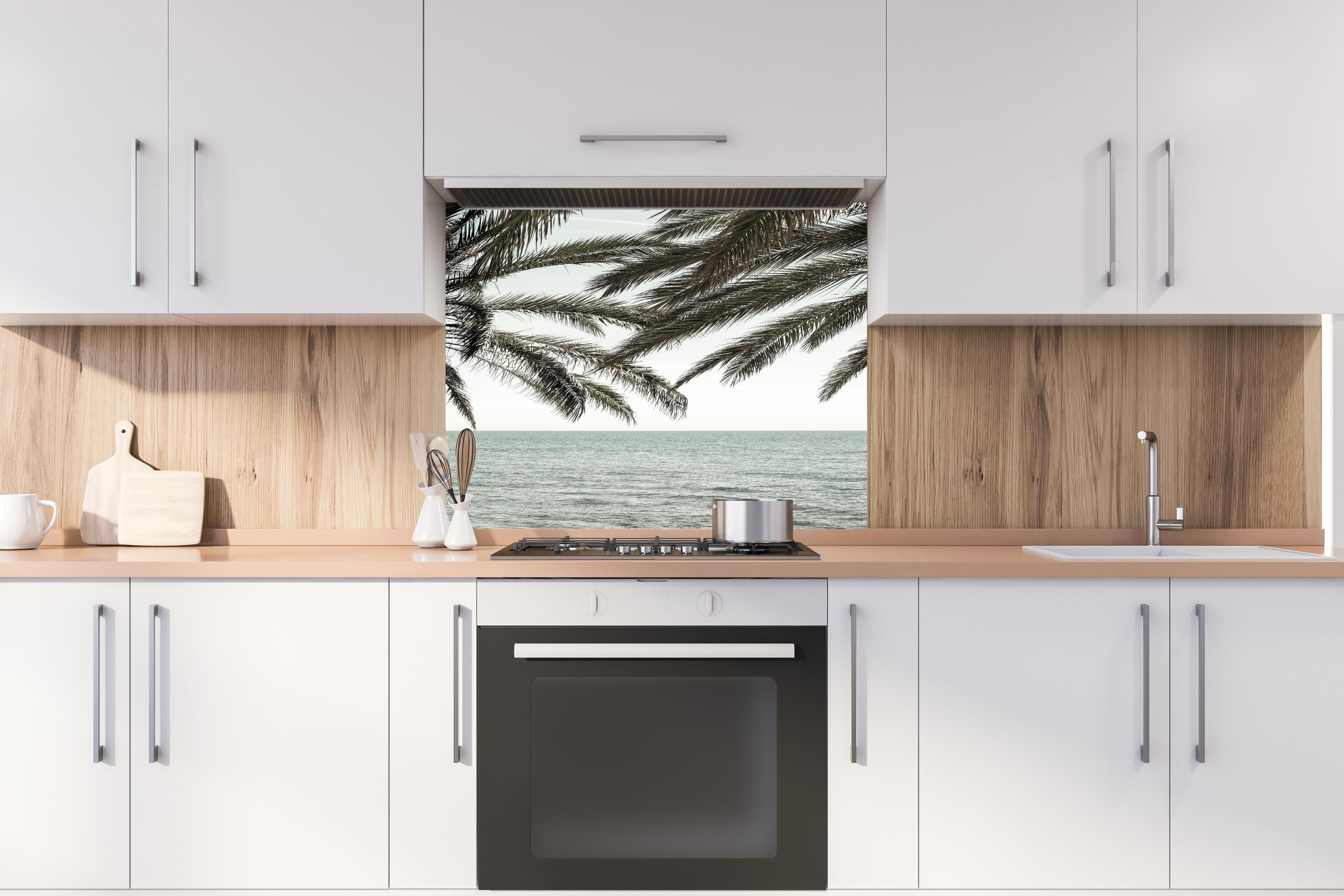 Spritzschutz - Palmen an der Küste  hinter einem Cerankochfeld zwischen Holz-Kochutensilien
