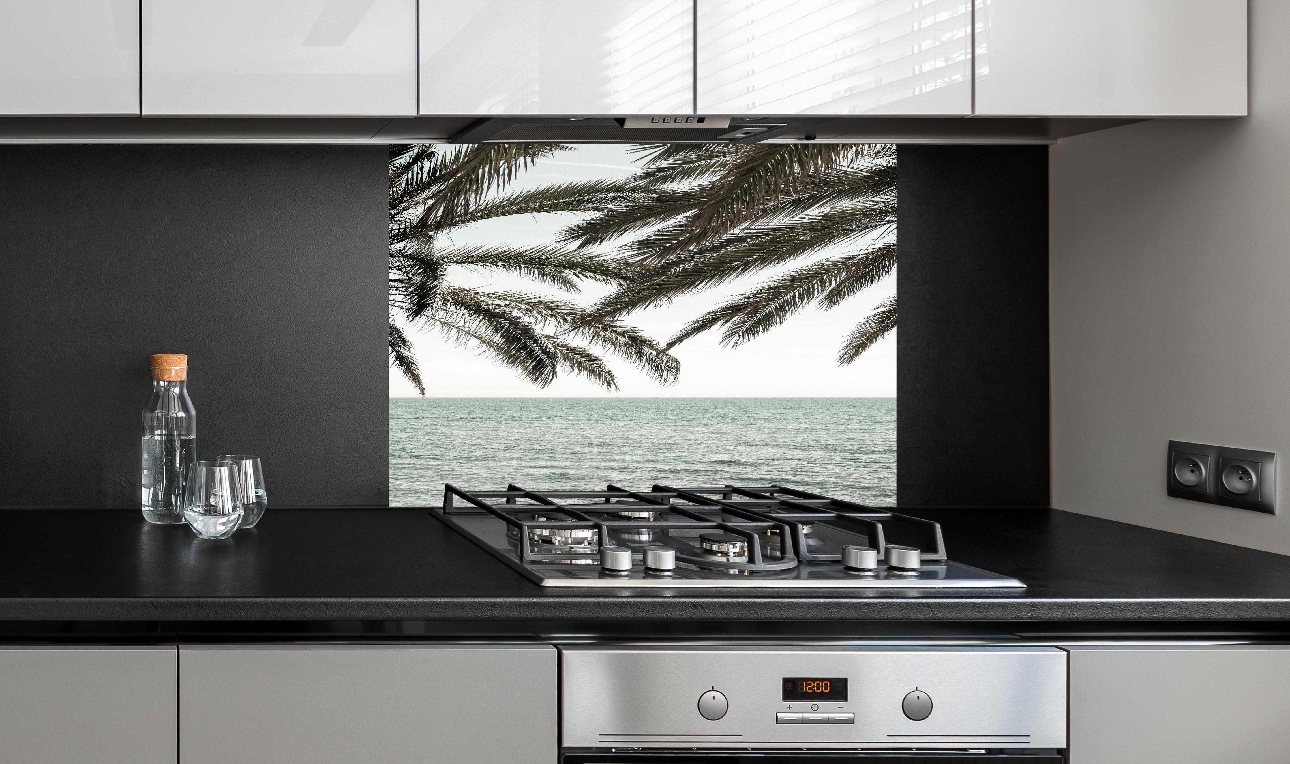 Spritzschutz - Palmen an der Küste  hinter einem Cerankochfeld zwischen Holz-Kochutensilien
