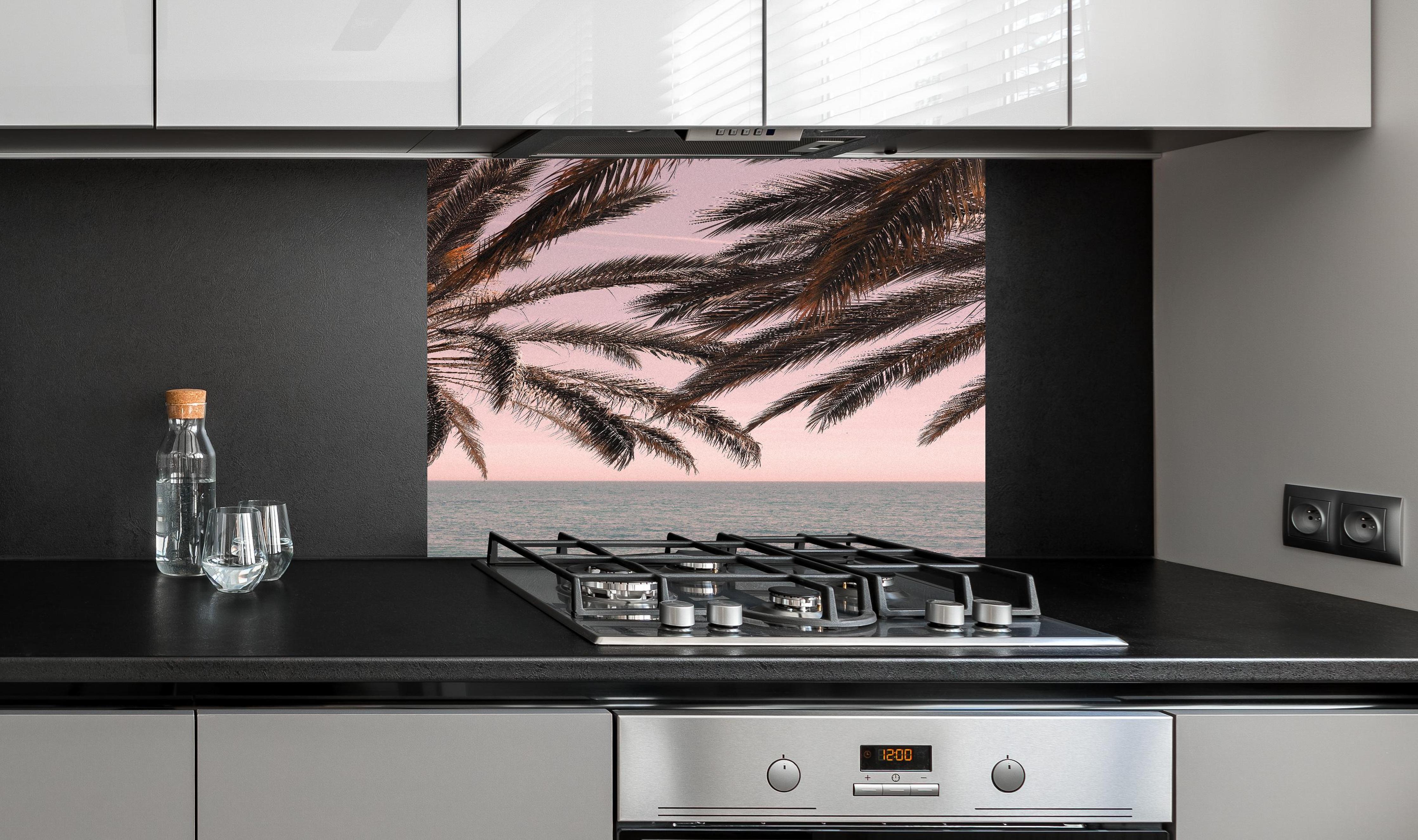 Spritzschutz - Palmen an der Küste hinter einem Cerankochfeld zwischen Holz-Kochutensilien
