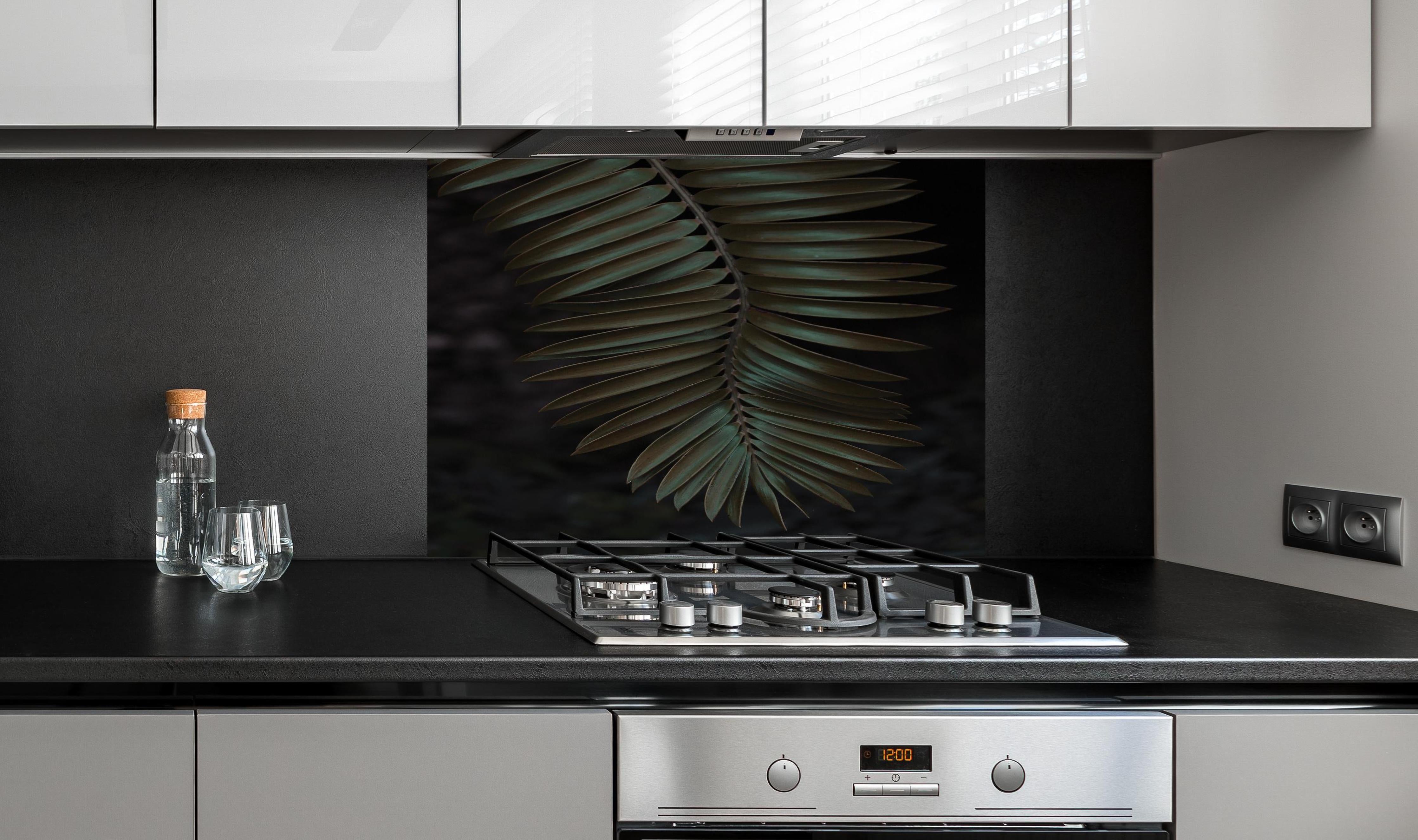 Spritzschutz - Palmenblätter hinter einem Cerankochfeld zwischen Holz-Kochutensilien
