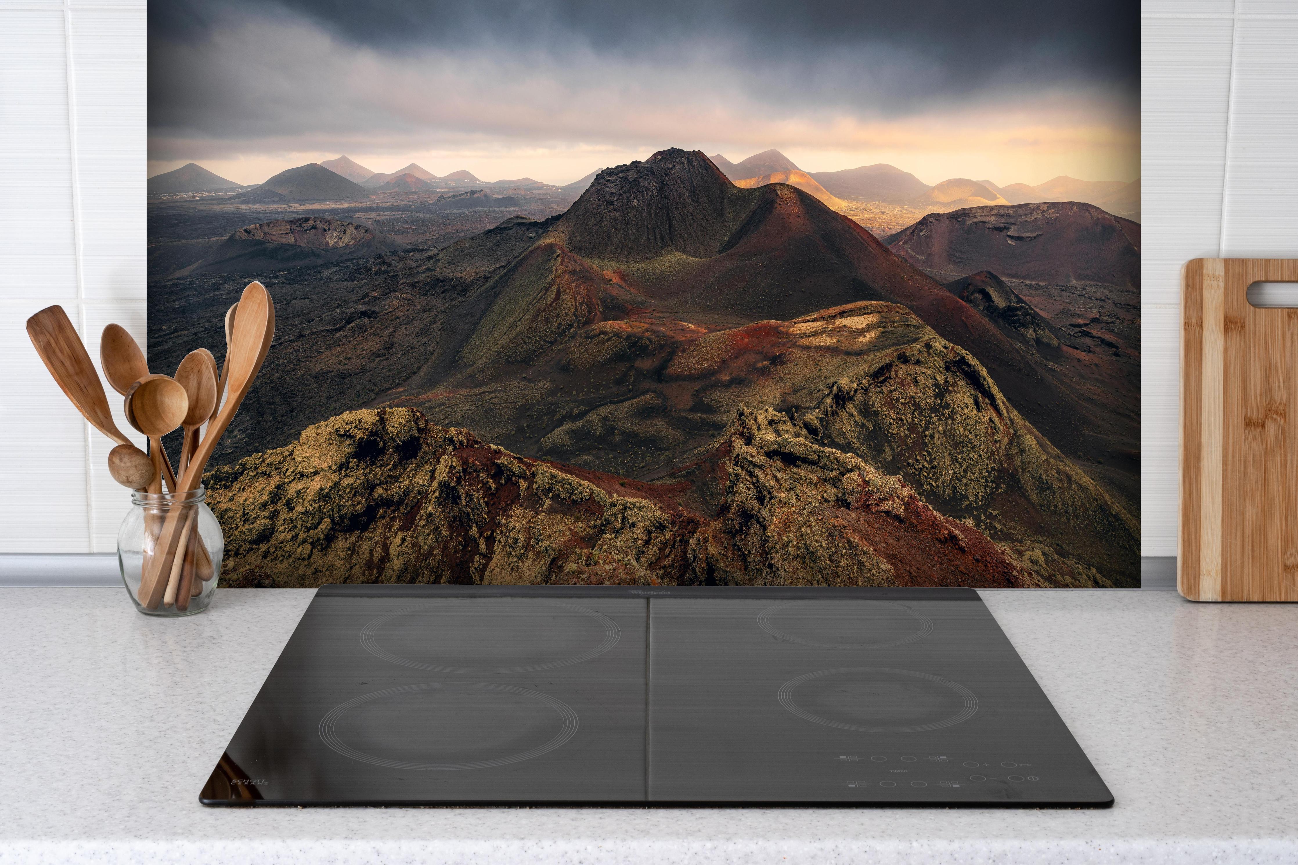 Spritzschutz - Panorama Vulkanberge unter dramatischem Himmel hinter einem Cerankochfeld zwischen Holz-Kochutensilien

