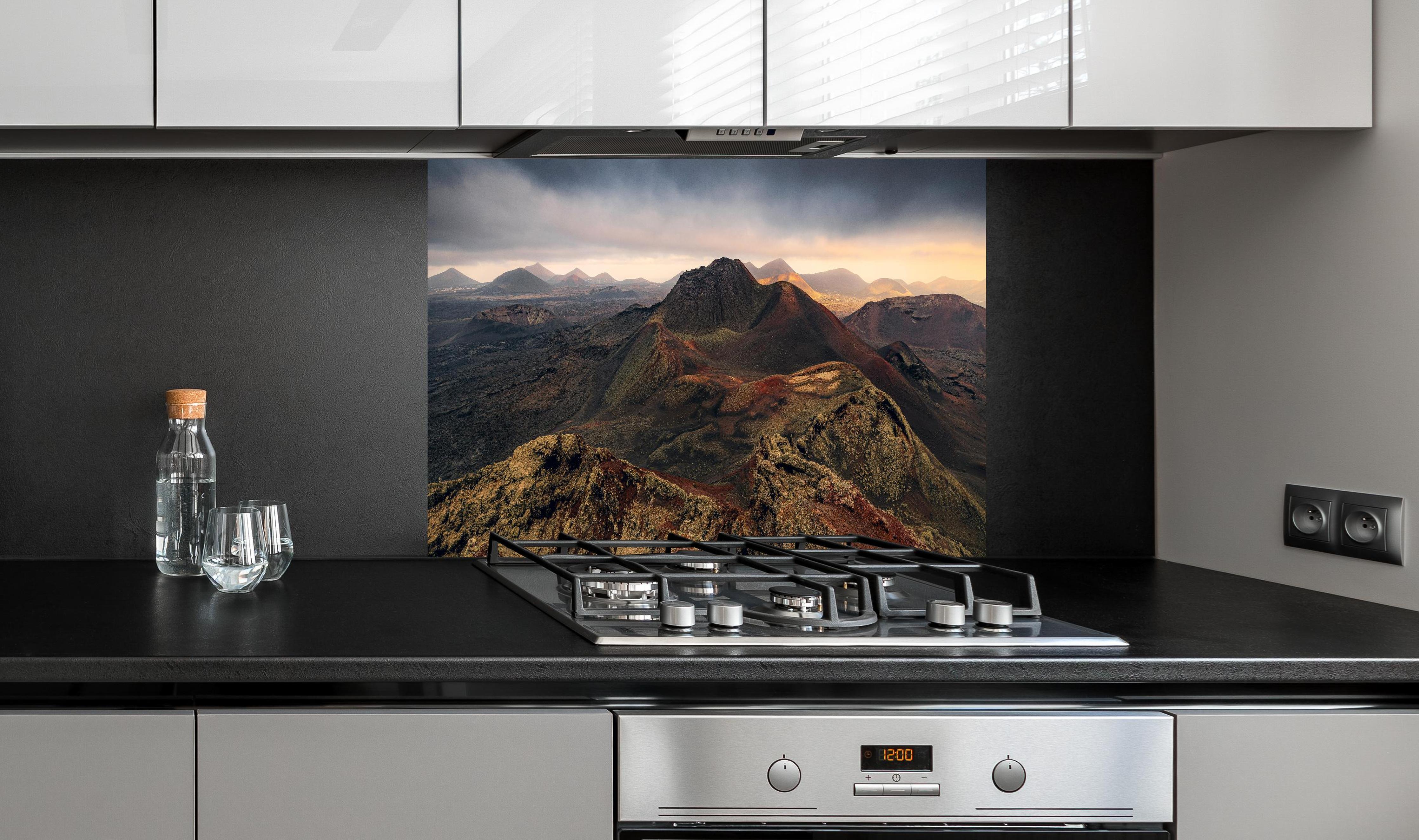 Spritzschutz - Panorama Vulkanberge unter dramatischem Himmel hinter einem Cerankochfeld zwischen Holz-Kochutensilien
