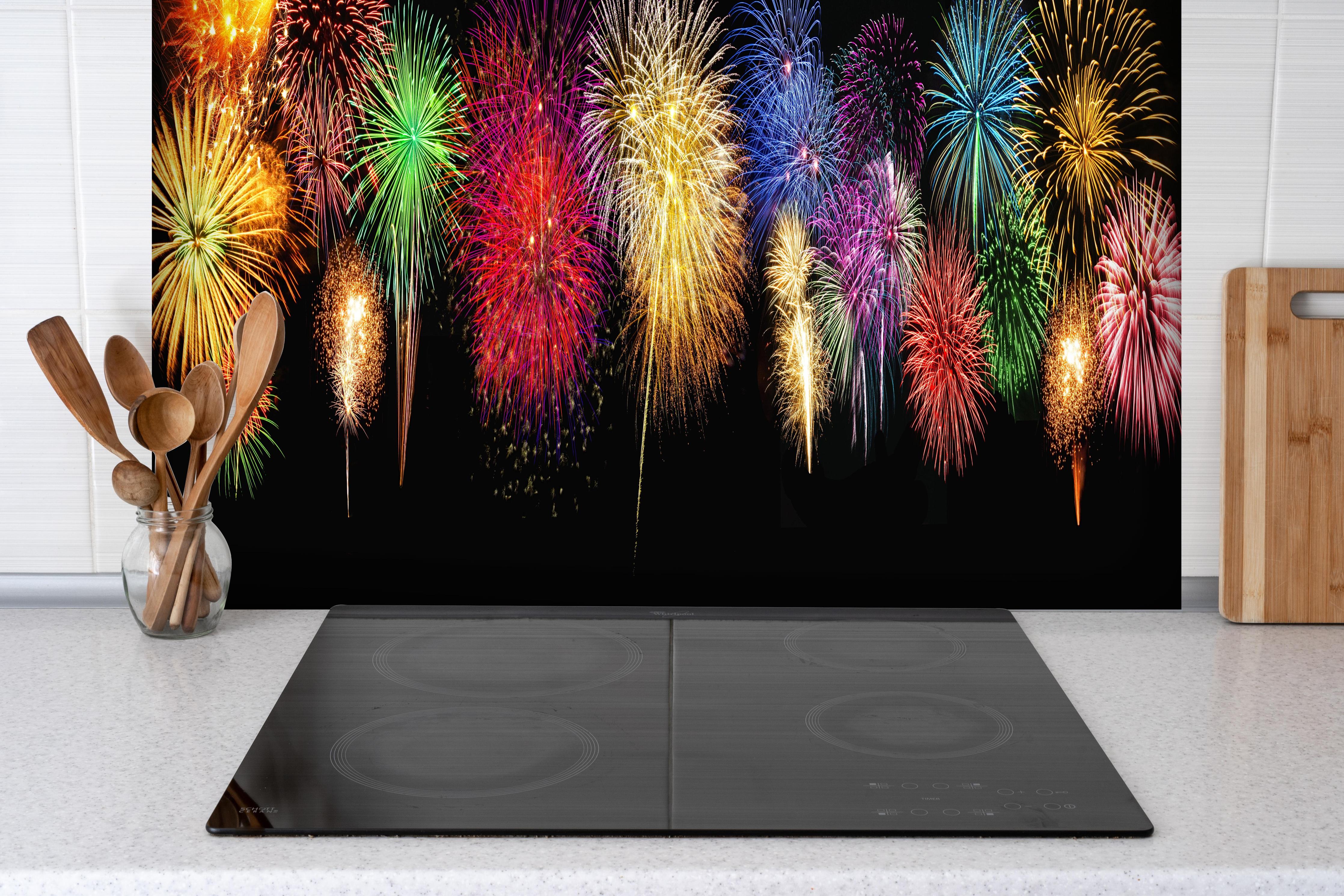 Spritzschutz - Panoramisches Silvesterfeuerwerk in leuchtenden Farben hinter einem Cerankochfeld zwischen Holz-Kochutensilien
