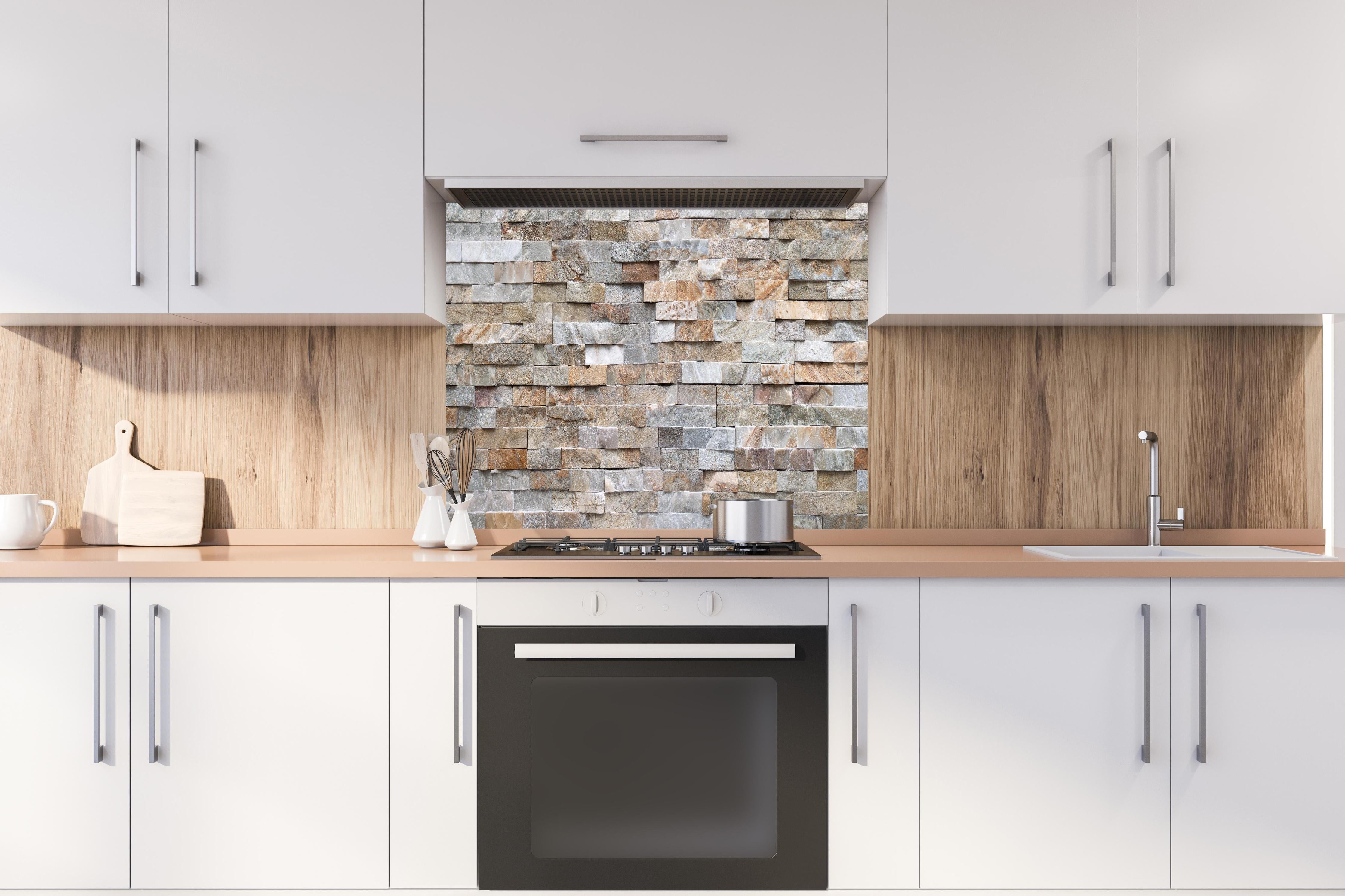 Spritzschutz - Pastellfarbige Steinmauer hinter einem Cerankochfeld zwischen Holz-Kochutensilien
