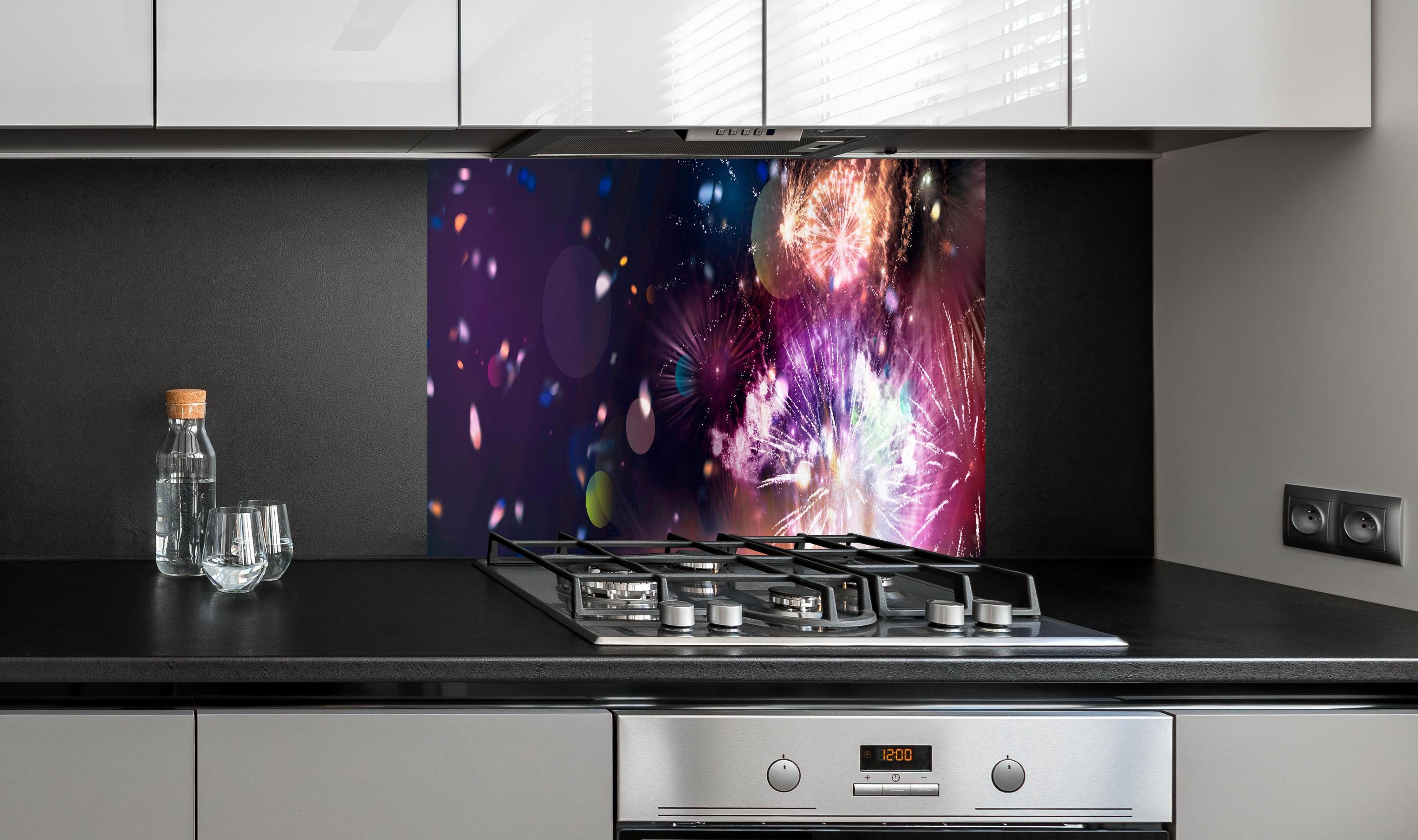 Spritzschutz - Prachtvolles Feuerwerk und schillerndes Konfetti hinter einem Cerankochfeld zwischen Holz-Kochutensilien
