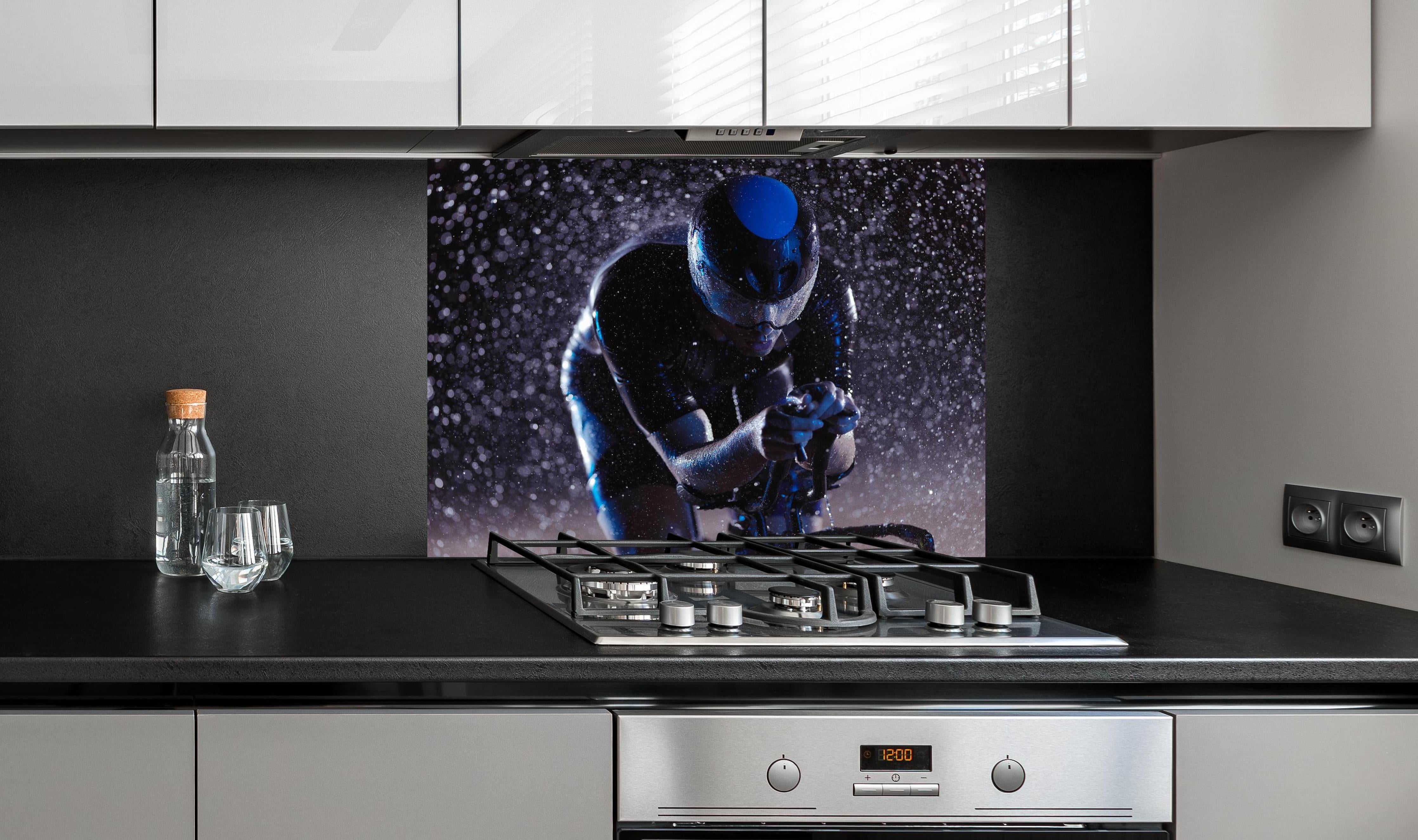 Spritzschutz - Radfahrer nachts bei Regen hinter einem Cerankochfeld zwischen Holz-Kochutensilien
