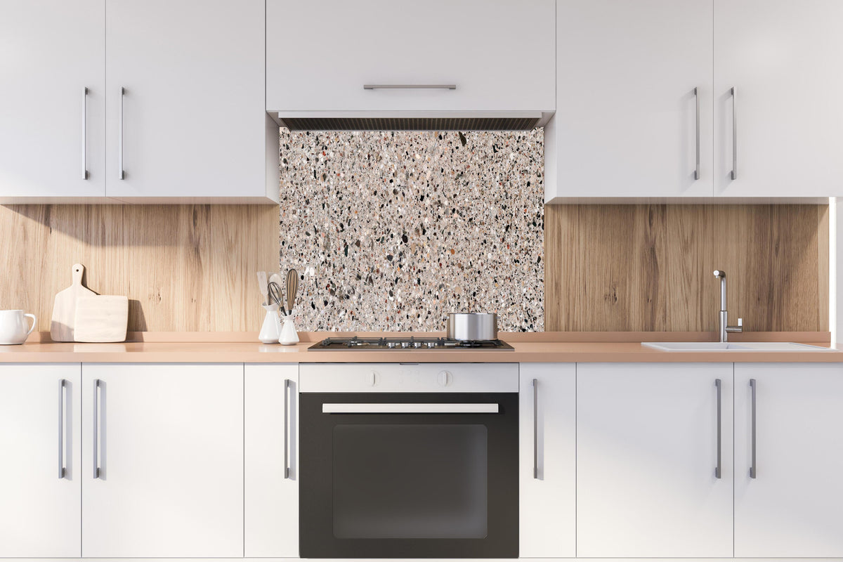 Spritzschutz - Robuste Beige Terrazzo Oberflächenstruktur hinter einem Cerankochfeld zwischen Holz-Kochutensilien
