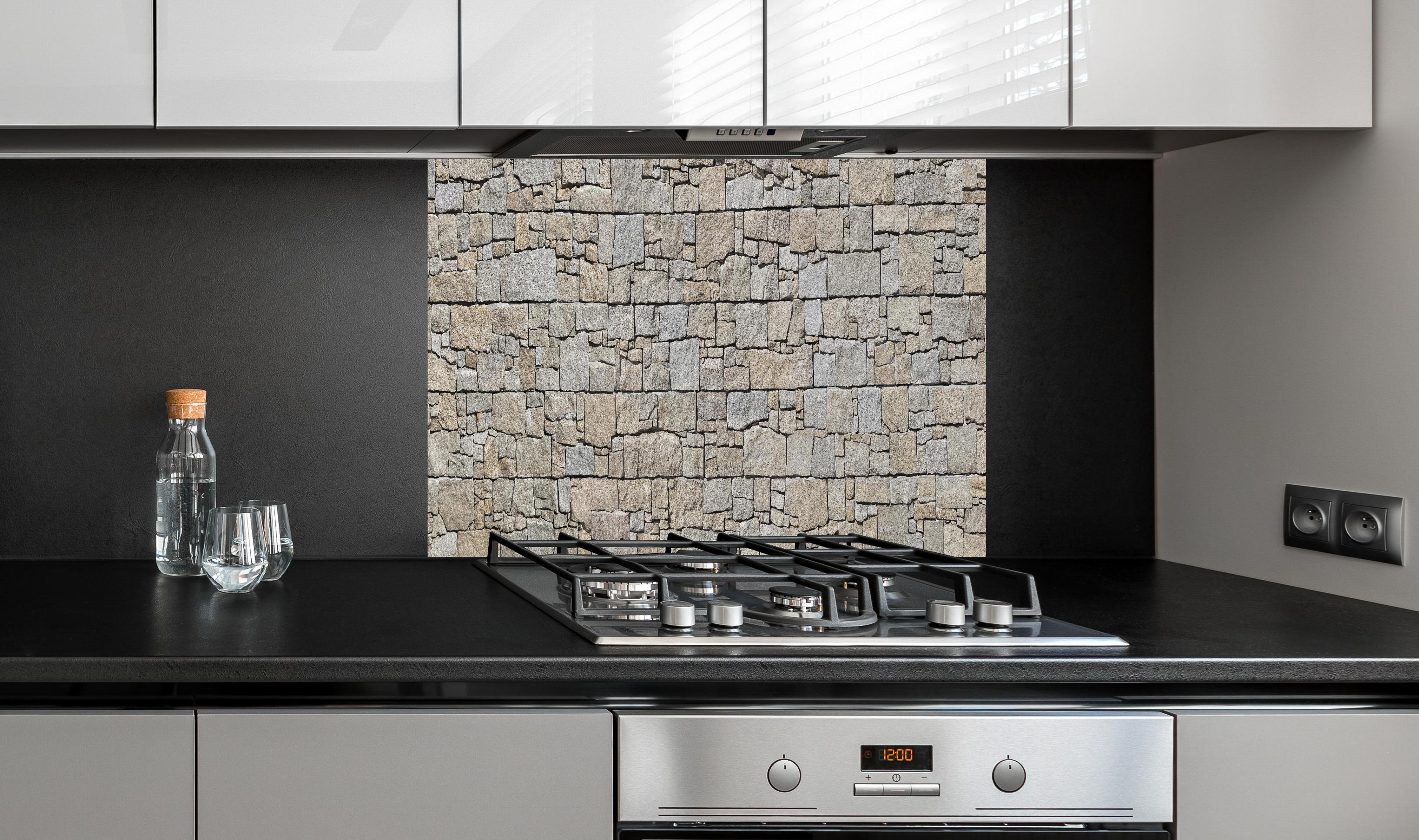 Spritzschutz - Robuste beige Natursteinmauertextur hinter einem Cerankochfeld zwischen Holz-Kochutensilien
