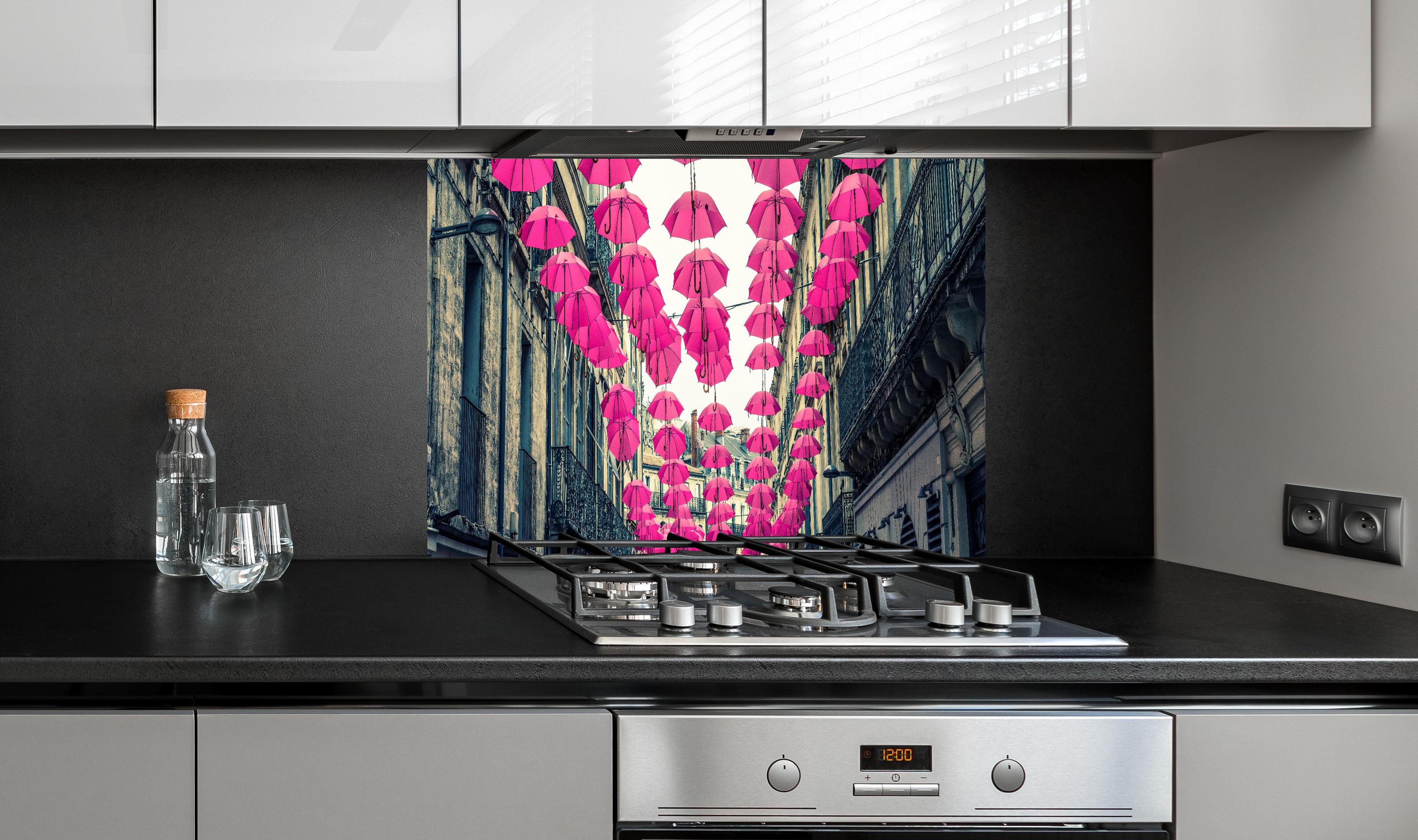 Spritzschutz - Rosafarbene Regenschirme als Straßenkunst hinter einem Cerankochfeld zwischen Holz-Kochutensilien
