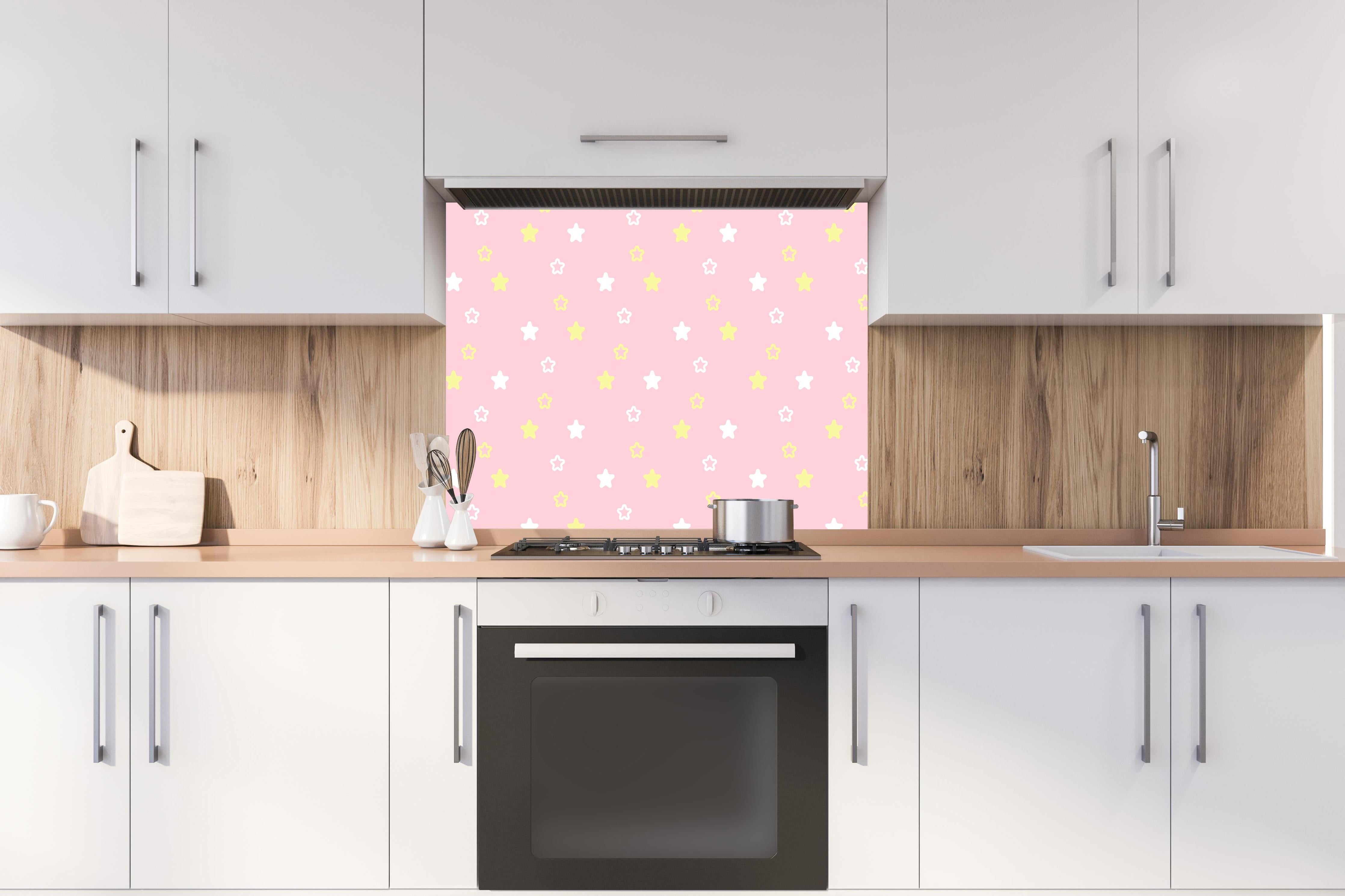 Spritzschutz - Rosafarbener Hintergrund mit gelben Sternen hinter einem Cerankochfeld zwischen Holz-Kochutensilien
