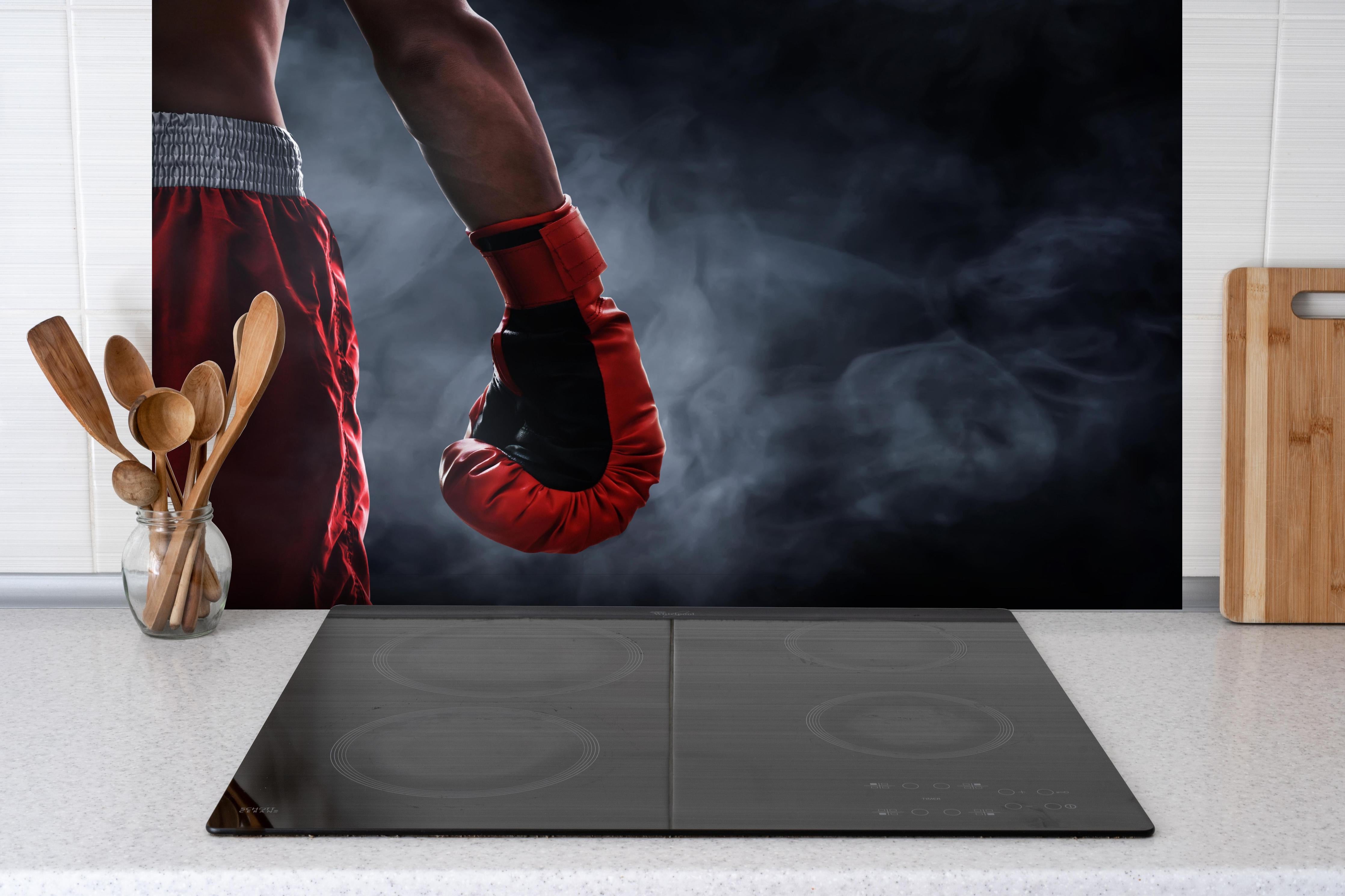 Spritzschutz - Roter Boxhandschuh hinter einem Cerankochfeld zwischen Holz-Kochutensilien
