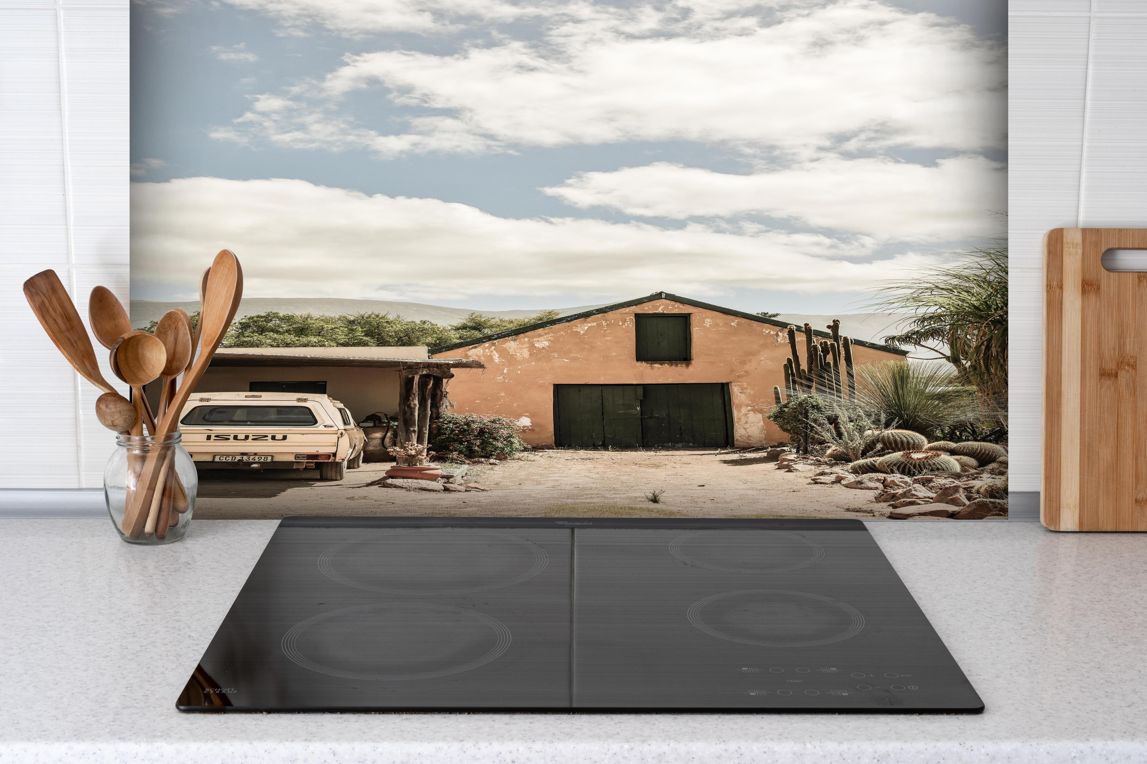 Spritzschutz - Rustikales Farmhaus Karoo in Ocker-Gelbtönen hinter einem Cerankochfeld zwischen Holz-Kochutensilien
