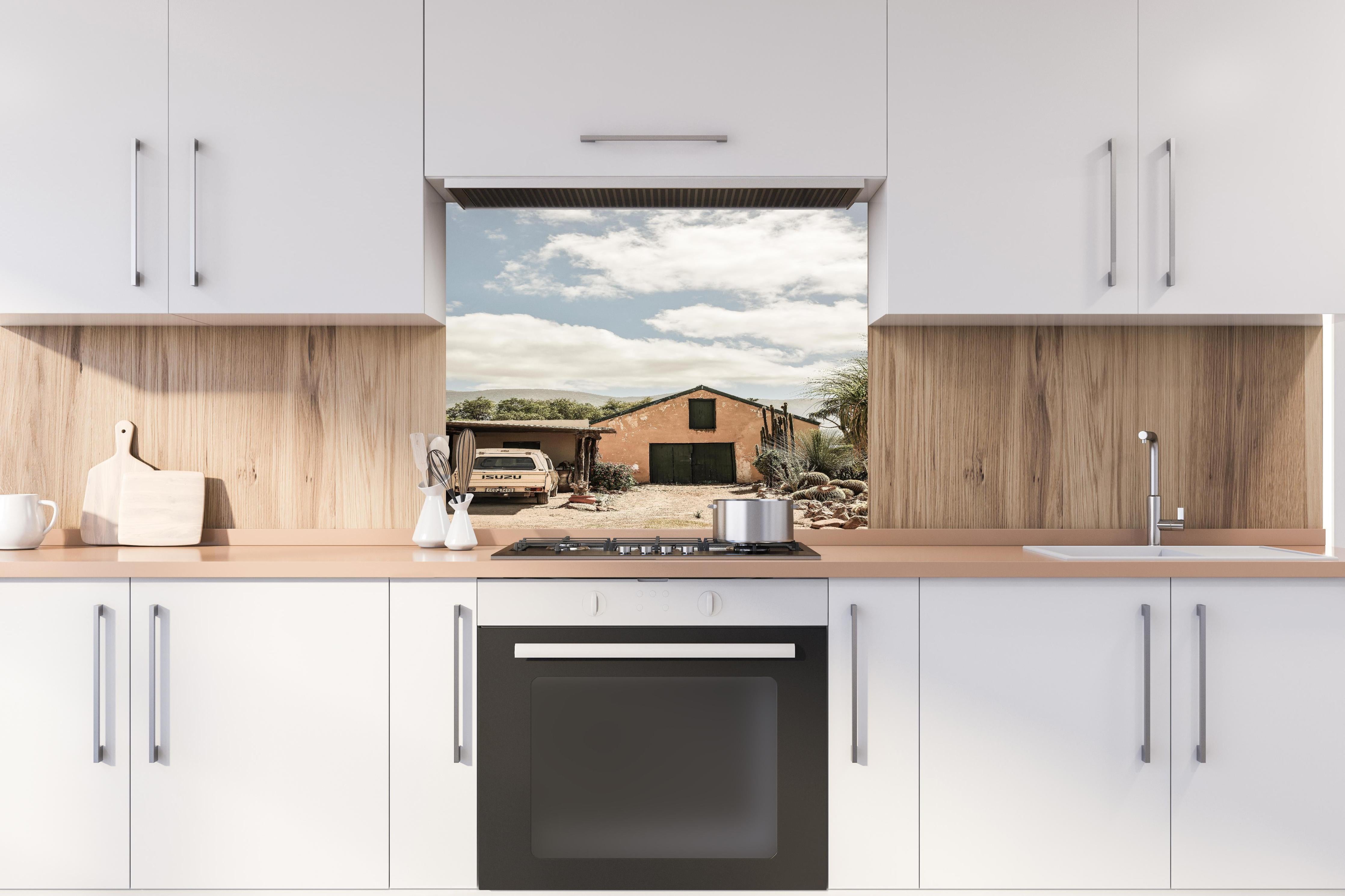 Spritzschutz - Rustikales Farmhaus Karoo in Ocker-Gelbtönen hinter einem Cerankochfeld zwischen Holz-Kochutensilien
