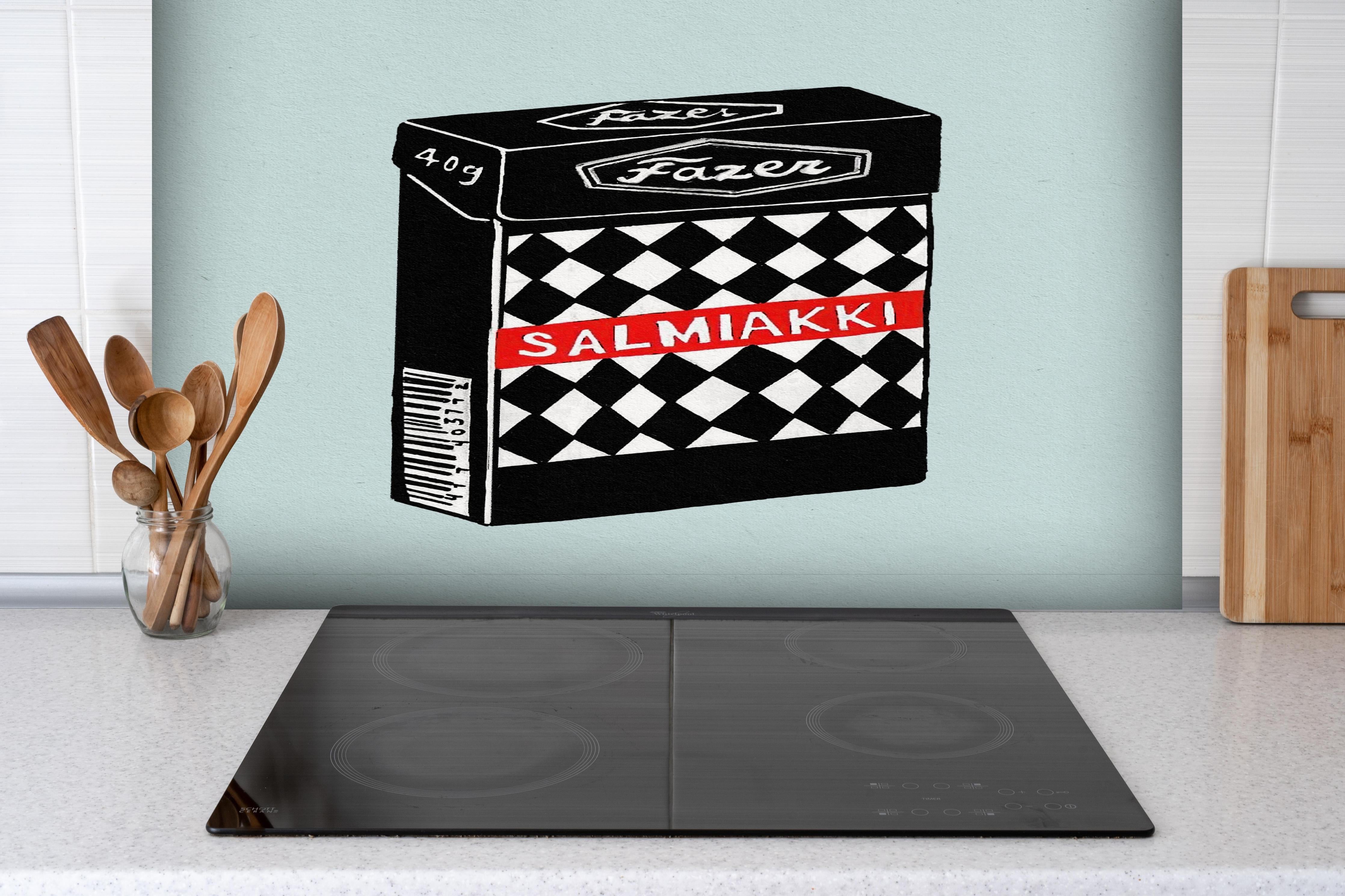 Spritzschutz - Salmiakki Schachtel hinter einem Cerankochfeld zwischen Holz-Kochutensilien
