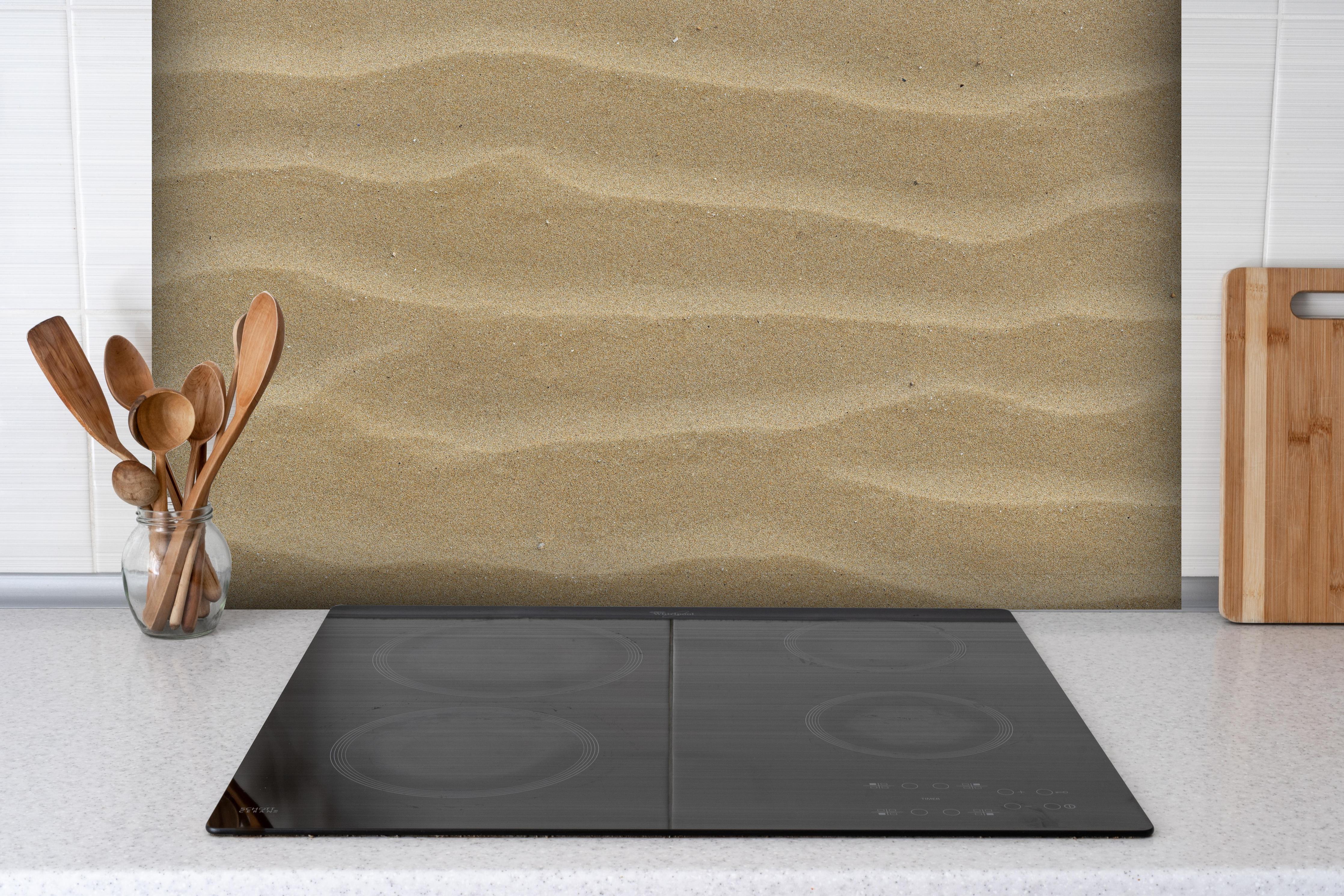 Spritzschutz - Sandstrand hinter einem Cerankochfeld zwischen Holz-Kochutensilien
