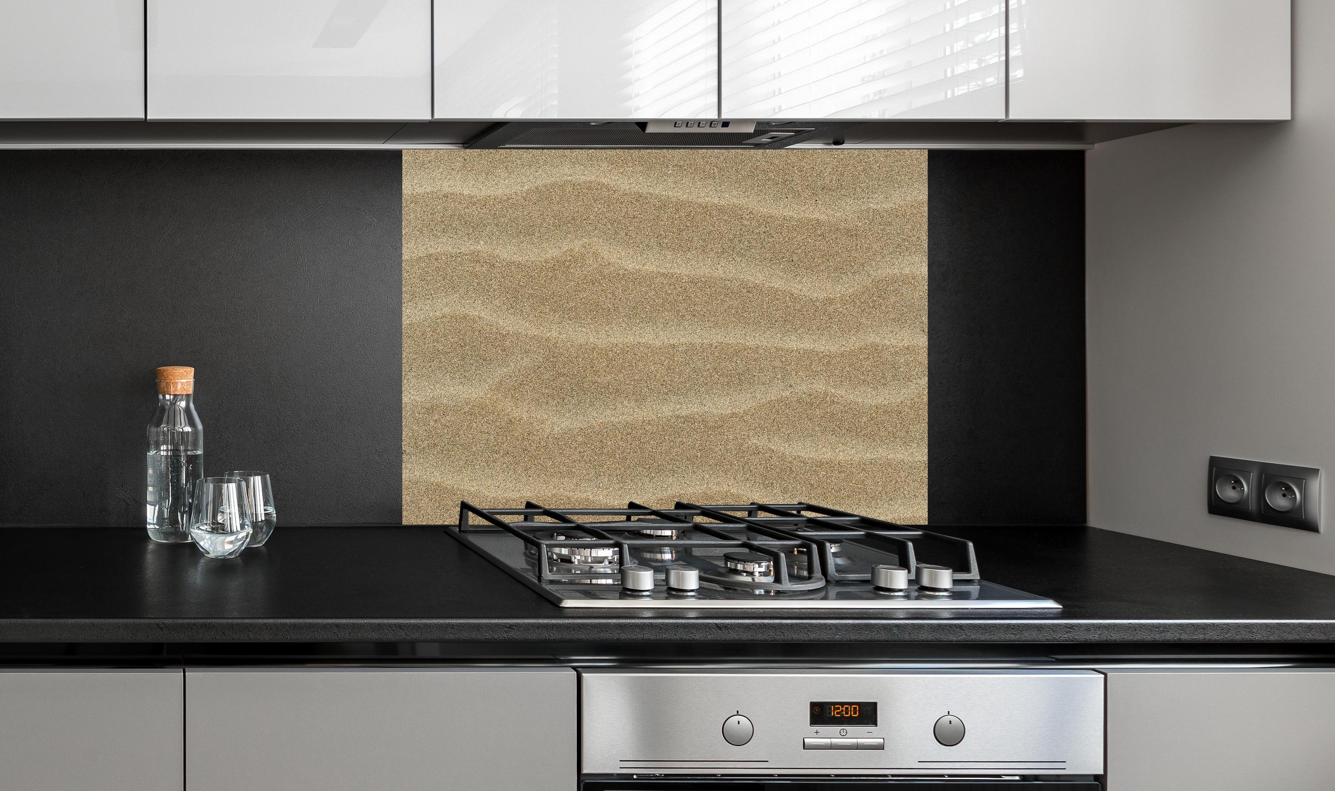 Spritzschutz - Sandstrand hinter einem Cerankochfeld zwischen Holz-Kochutensilien
