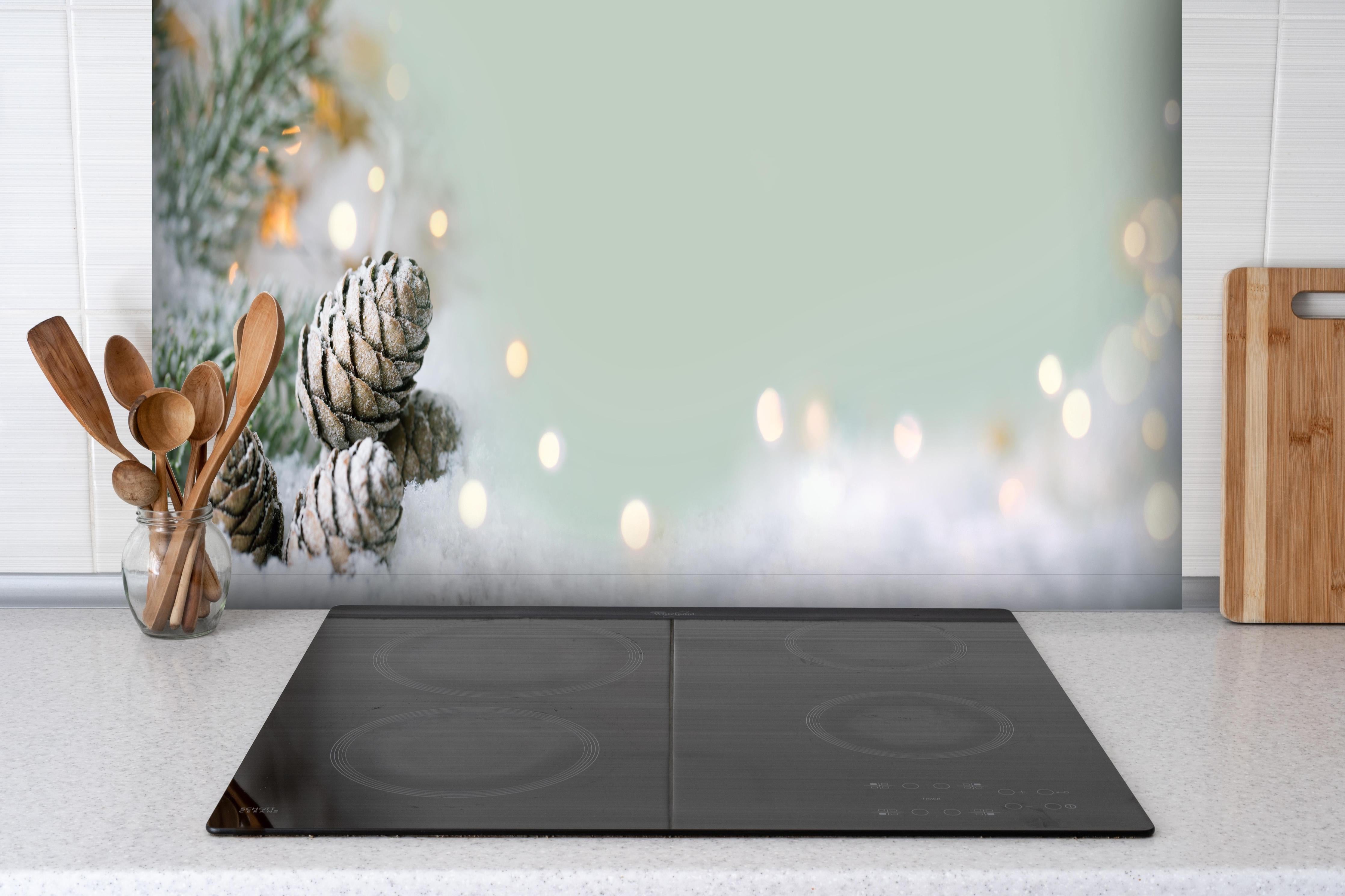 Spritzschutz - Schneelandschaft zu Weihnachten hinter einem Cerankochfeld zwischen Holz-Kochutensilien
