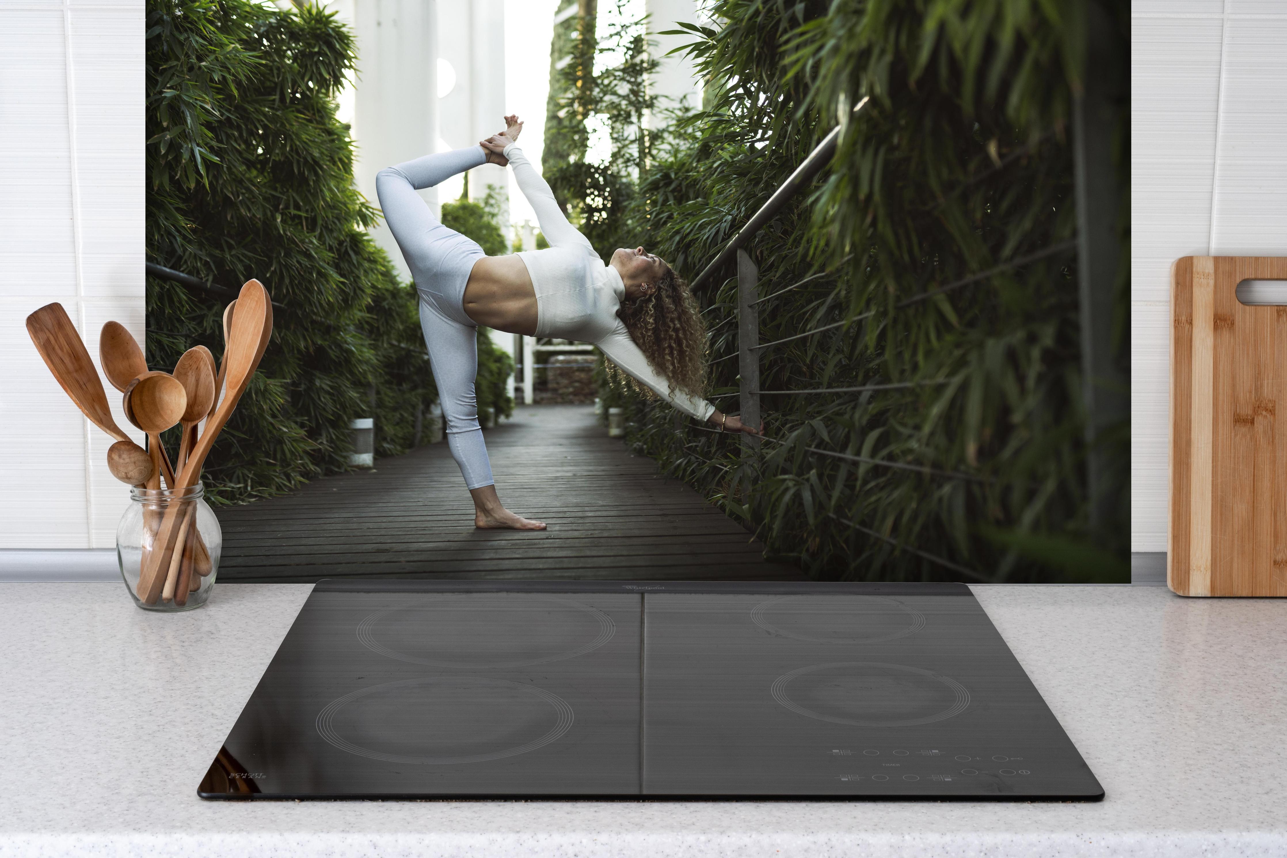 Spritzschutz - Schöne blonde Frau mit lockigem Haar hinter einem Cerankochfeld zwischen Holz-Kochutensilien
