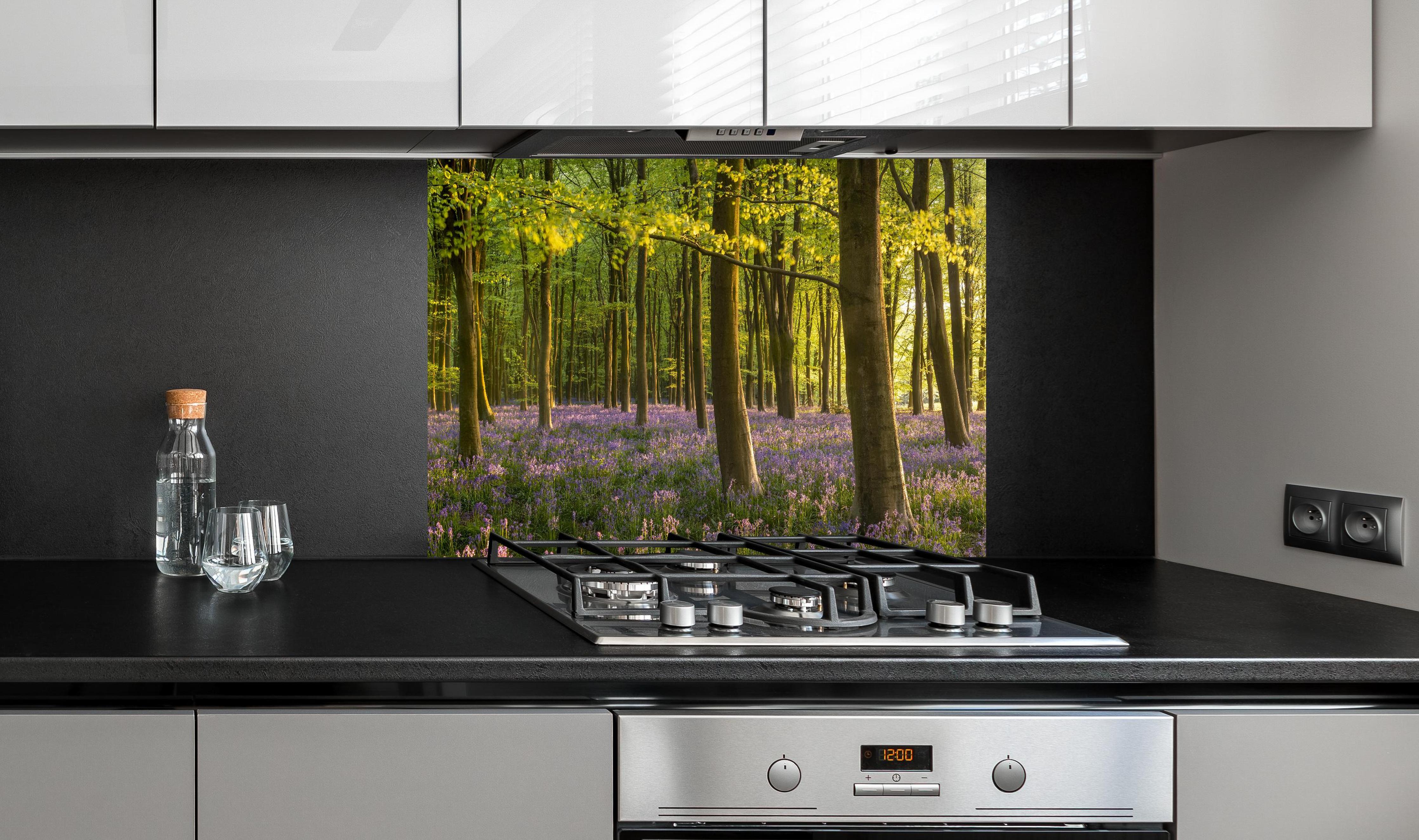 Spritzschutz - Schöner Blauglockenwald hinter einem Cerankochfeld zwischen Holz-Kochutensilien
