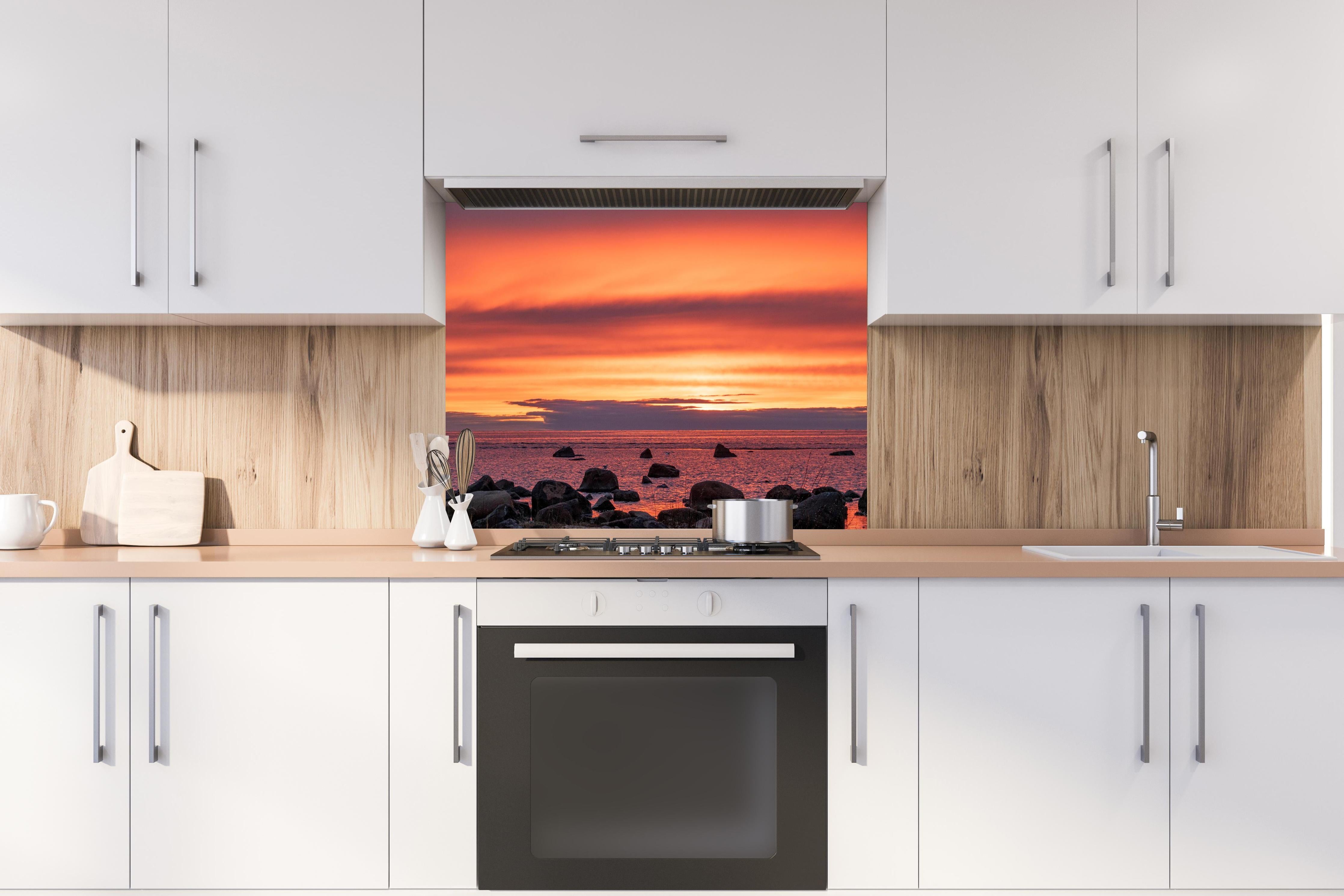 Spritzschutz - Schöner Sonnenuntergang am Meer hinter einem Cerankochfeld zwischen Holz-Kochutensilien
