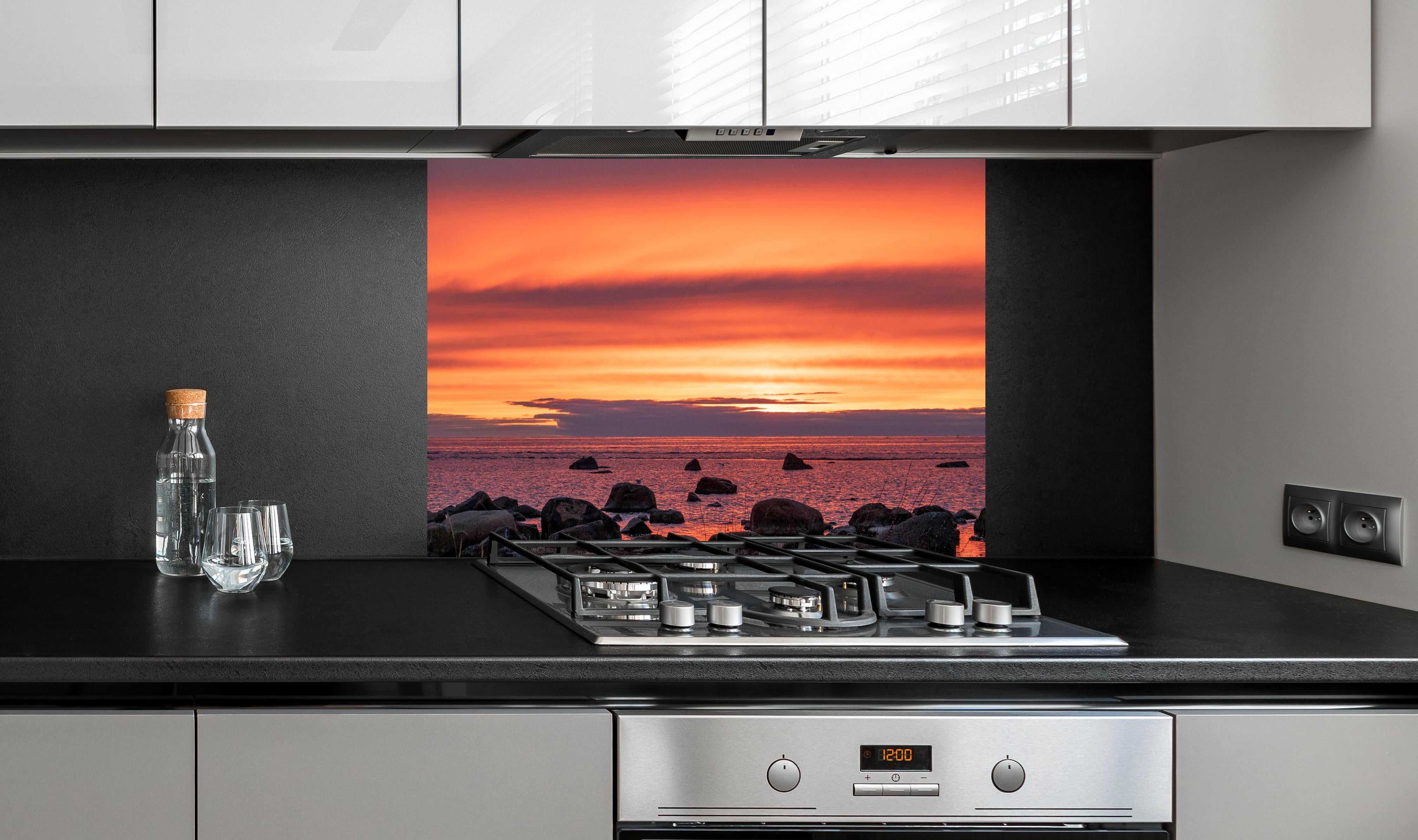 Spritzschutz - Schöner Sonnenuntergang am Meer hinter einem Cerankochfeld zwischen Holz-Kochutensilien
